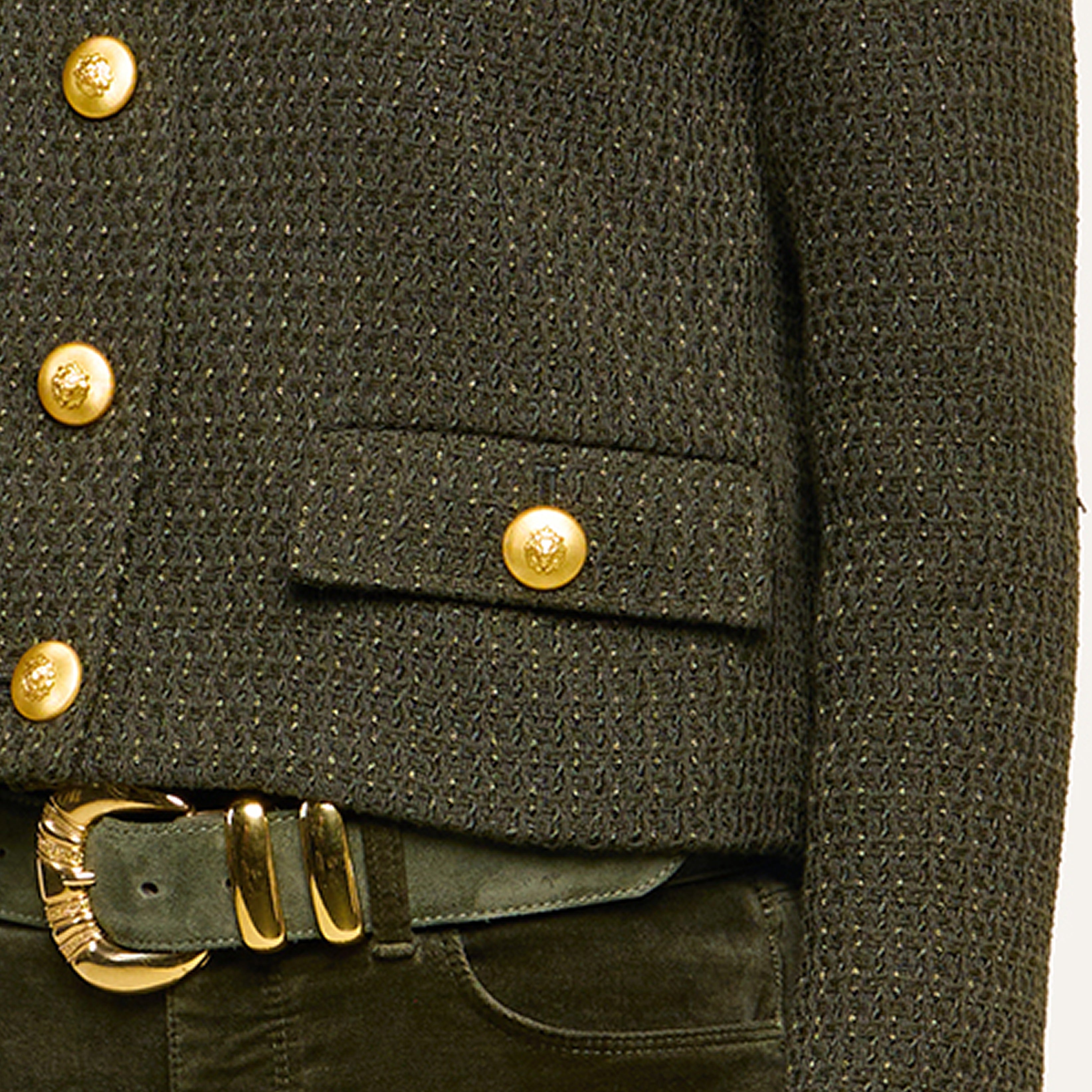 Close-up of a textured dark green jacket with gold buttons, paired with matching green pants and a gold-buckled belt. The ensemble features a sophisticated and elegant style.