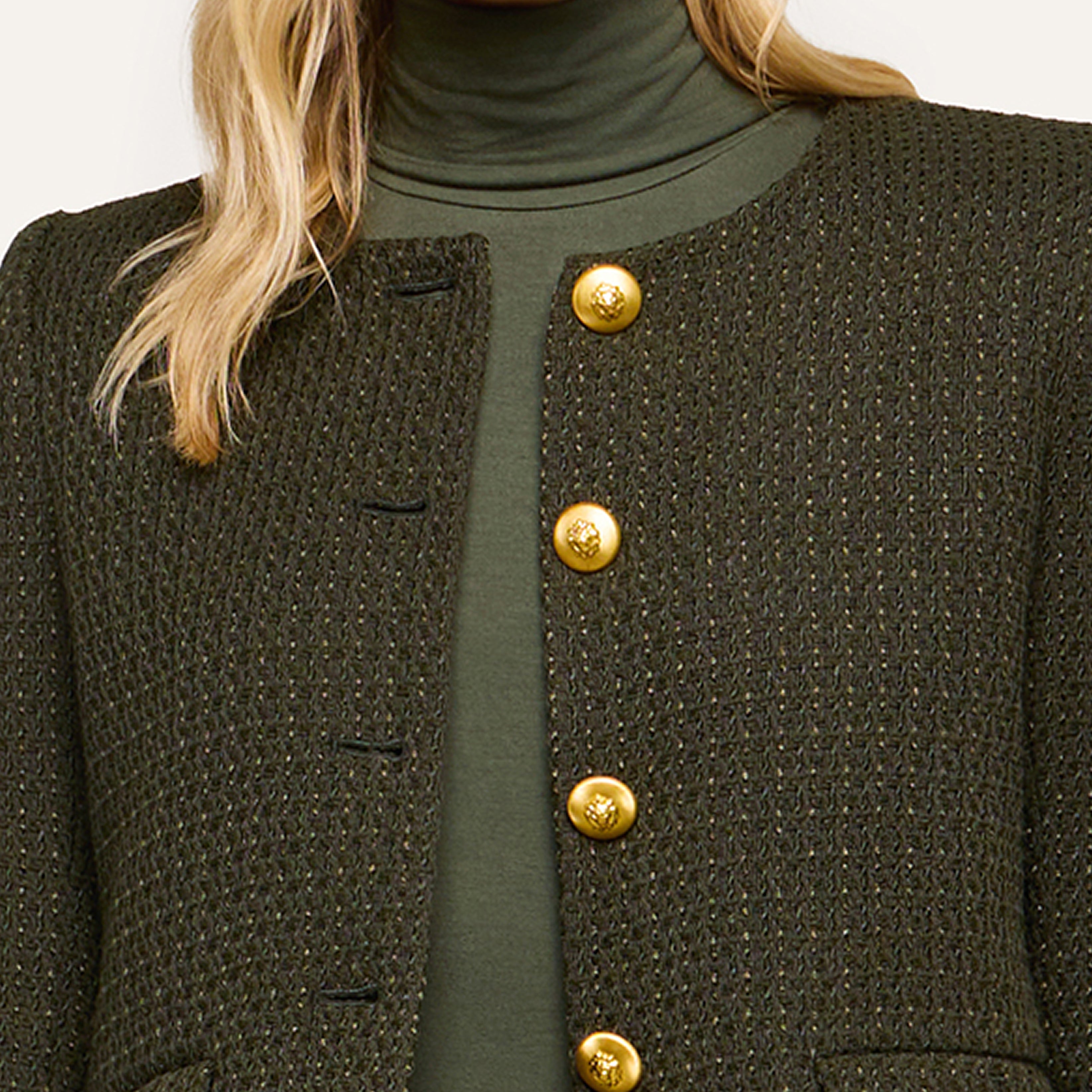 A person wearing a textured, dark green jacket with four gold buttons over a green turtleneck is shown; only the lower face and upper torso are visible in this portrait.
