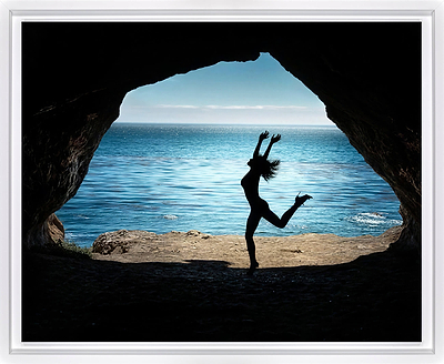 A framed photographic print showing a silhouetted dancer jumping in front of a cave opening that reveals a bright blue ocean and sky.