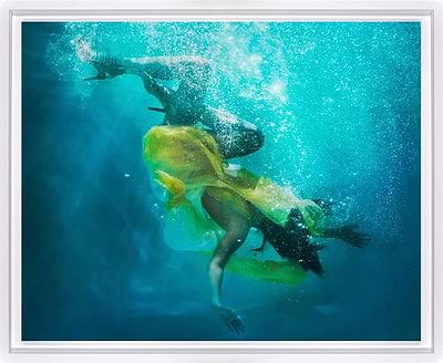 Underwater art print featuring a swimmer in a bright yellow swimsuit swimming through turquoise blue water with rising bubbles, presented in a white frame.