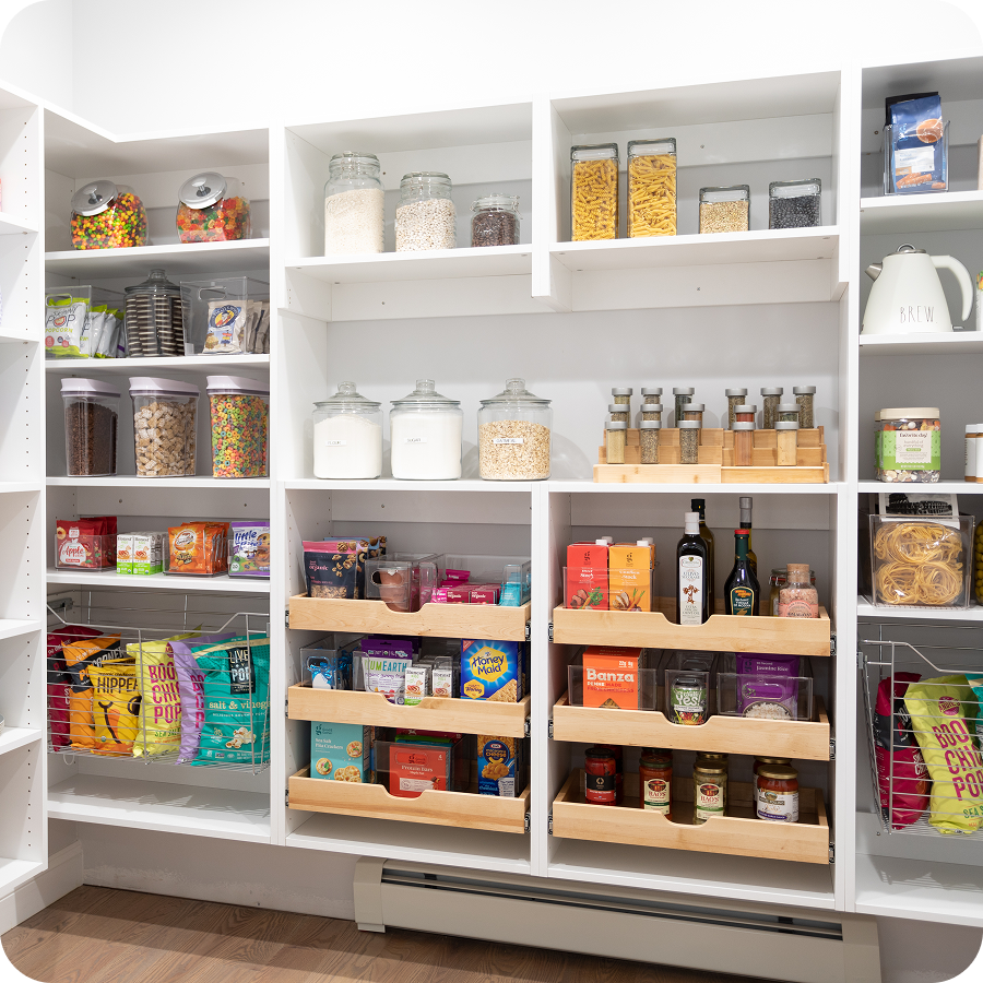 White pantry featuring wooden wooden shelf-pull out drawers, wire baskets, & open storage with snacks, jars, & other food items