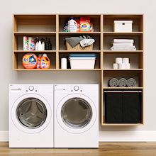 Natural Oak Select Laundry Kit featuring a built-in pull-out hamper and upper shelves installed above a washer and dryer to organize everyday laundry essentials.