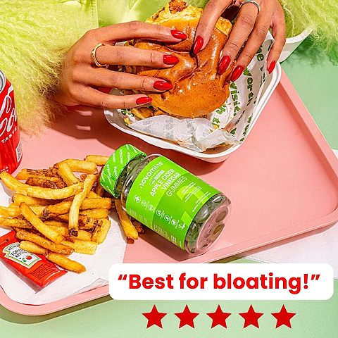 Lady eating a burger with a bottle of ACV gummies on her tray.