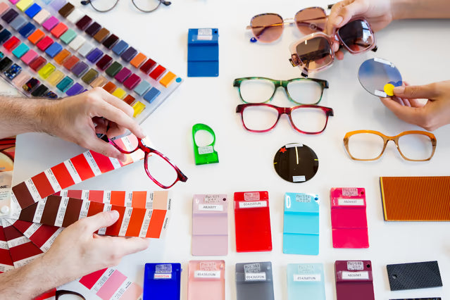 Color swatches and eyeglasses on a table with hands interacting with the items.