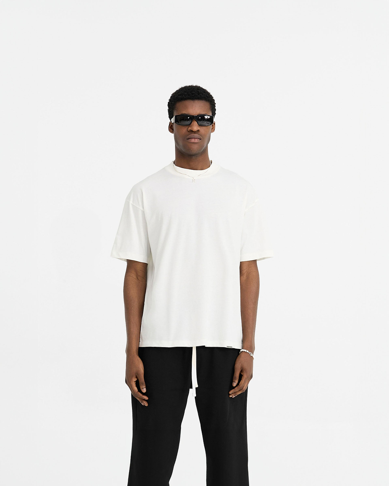 Man wearing a white oversized t-shirt on a plain white background | Initial Oversized T-Shirt in Flat White | Oversized t-shirt with embroidered Initial and metal bar detailing | Initial T-Shirts | Represent Clo