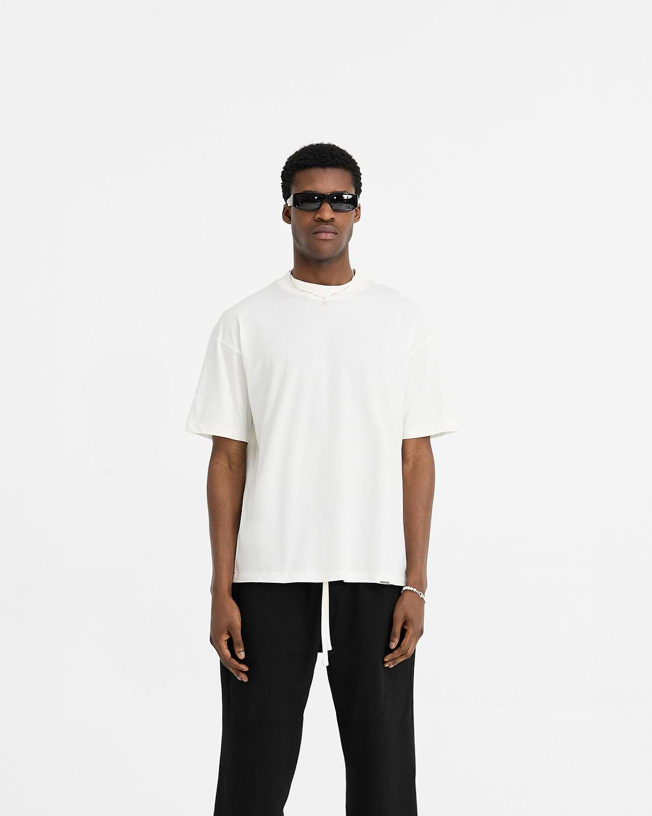 Man wearing a white oversized t-shirt on a plain white background | Initial Oversized T-Shirt in Flat White | Oversized t-shirt with embroidered Initial and metal bar detailing | Initial T-Shirts | Represent Clo