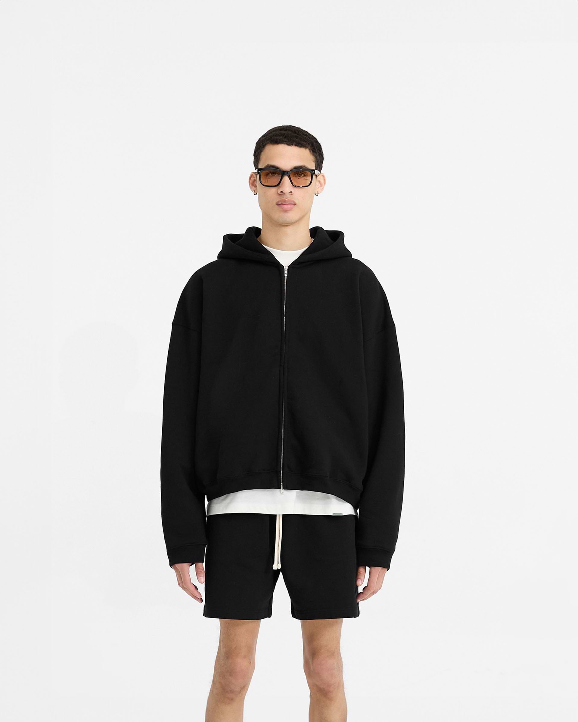 Man wearing a black oversized hoodie on a plain white background | Initial Boxy Zip Through Hoodie in Black | Heavyweight boxy zip hoodie with cropped body | Initial Hoodies | Represent Clo