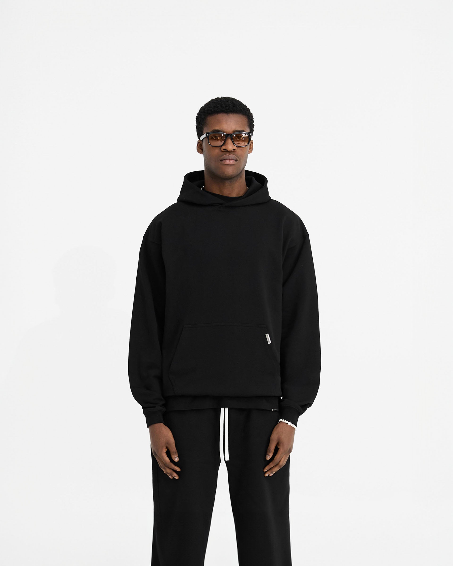 Man wearing a black oversized hoodie on a plain white background | Initial Oversized Hoodie in Black | Heavyweight loopback jersey cotton hoodie | Initial Hoodies | Represent Clo