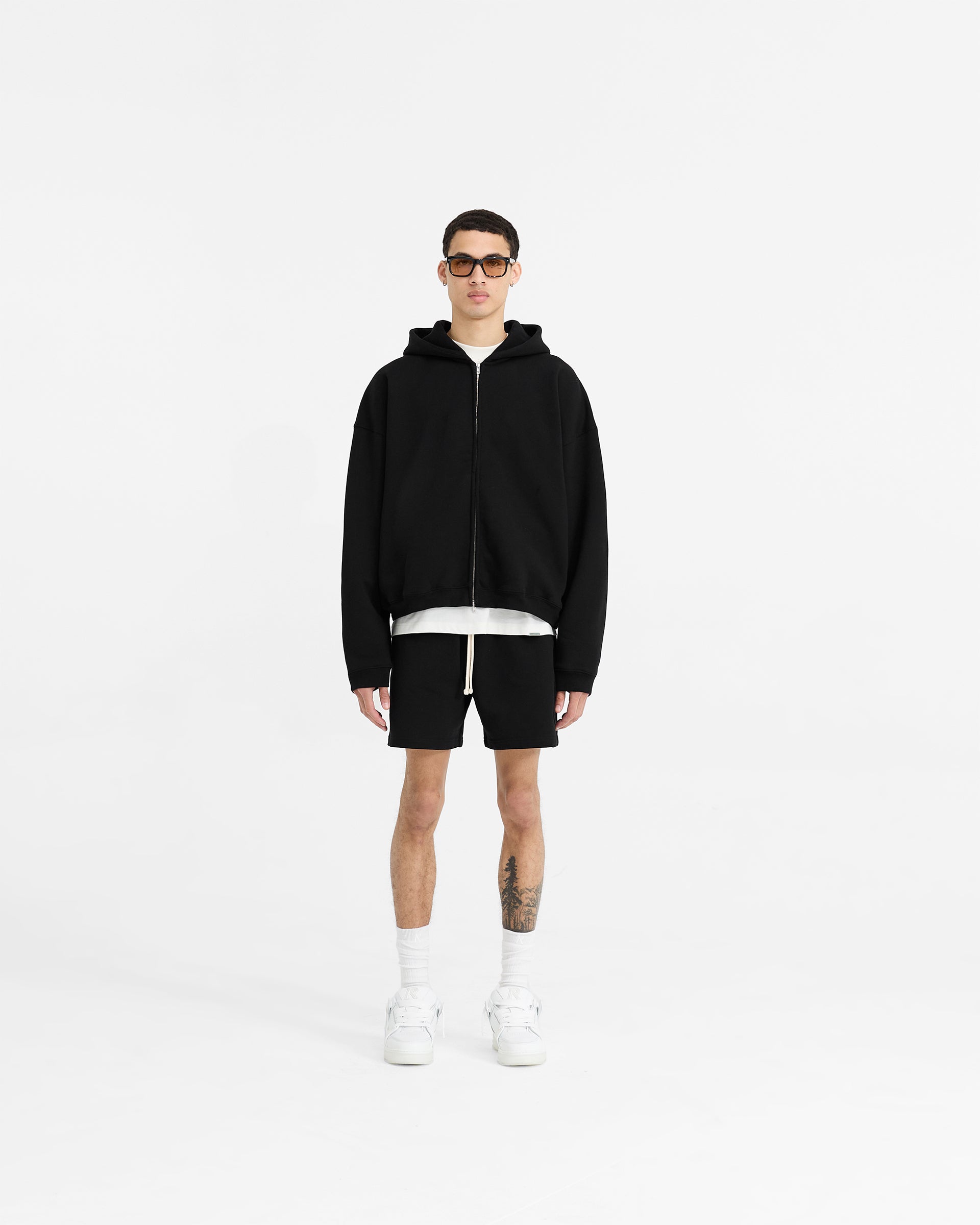 Man wearing a black oversized zip hoodie on a plain white background | Initial Boxy Zip Through Hoodie in Black | Boxy fit zip hoodie with dropped shoulders | Initial Hoodies | Represent Clo