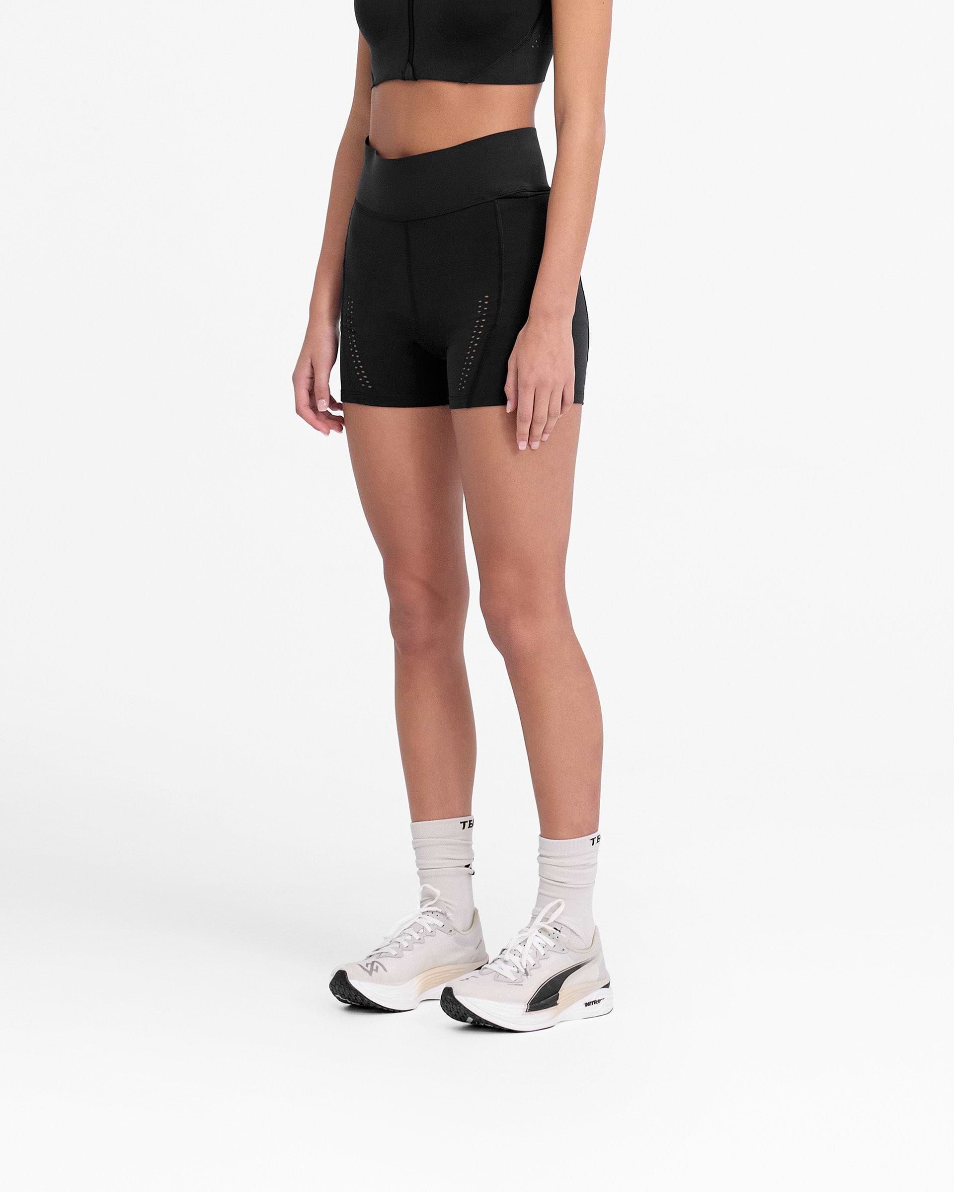 Woman wearing black legging shorts on a plain white background | 247 X Puma Women's Shapeluxe Legging Short in Black | High waisted shorts with bonded waistband and laser cut details | 247 Shorts | Represent Clo