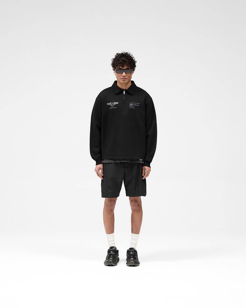 Man wearing an oversized black sweater with vintage graphics on a plain white background | Team Rep Quarter Zip in Jet Black | Quarter zip sweater with Represent branded zip | SS25 Sweaters | Represent Clo
