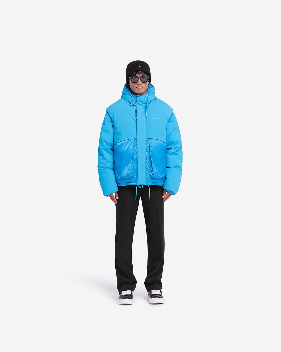 Man wearing an electric blue puffer jacket on a plain white background | Layered Hooded Puffer in Electric Blue | Duck down jacket with adjustable hood | FW24 Outerwear | Represent Clo