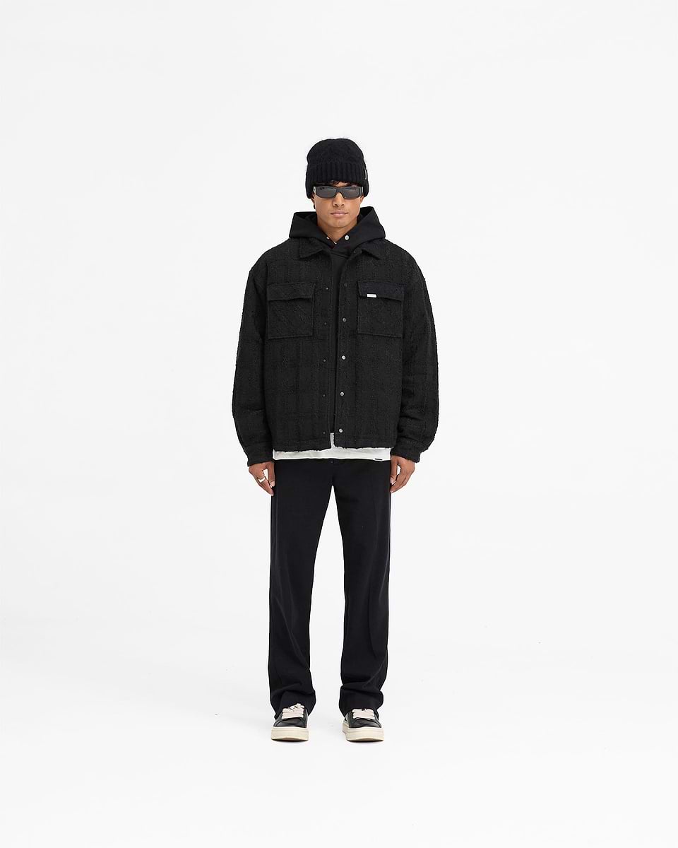 Man wearing a black overshirt on a plain white background | Wadded Overshirt in Black | Oversized black overshirt with matte popper closures | FW24 Shirts | Represent Clo