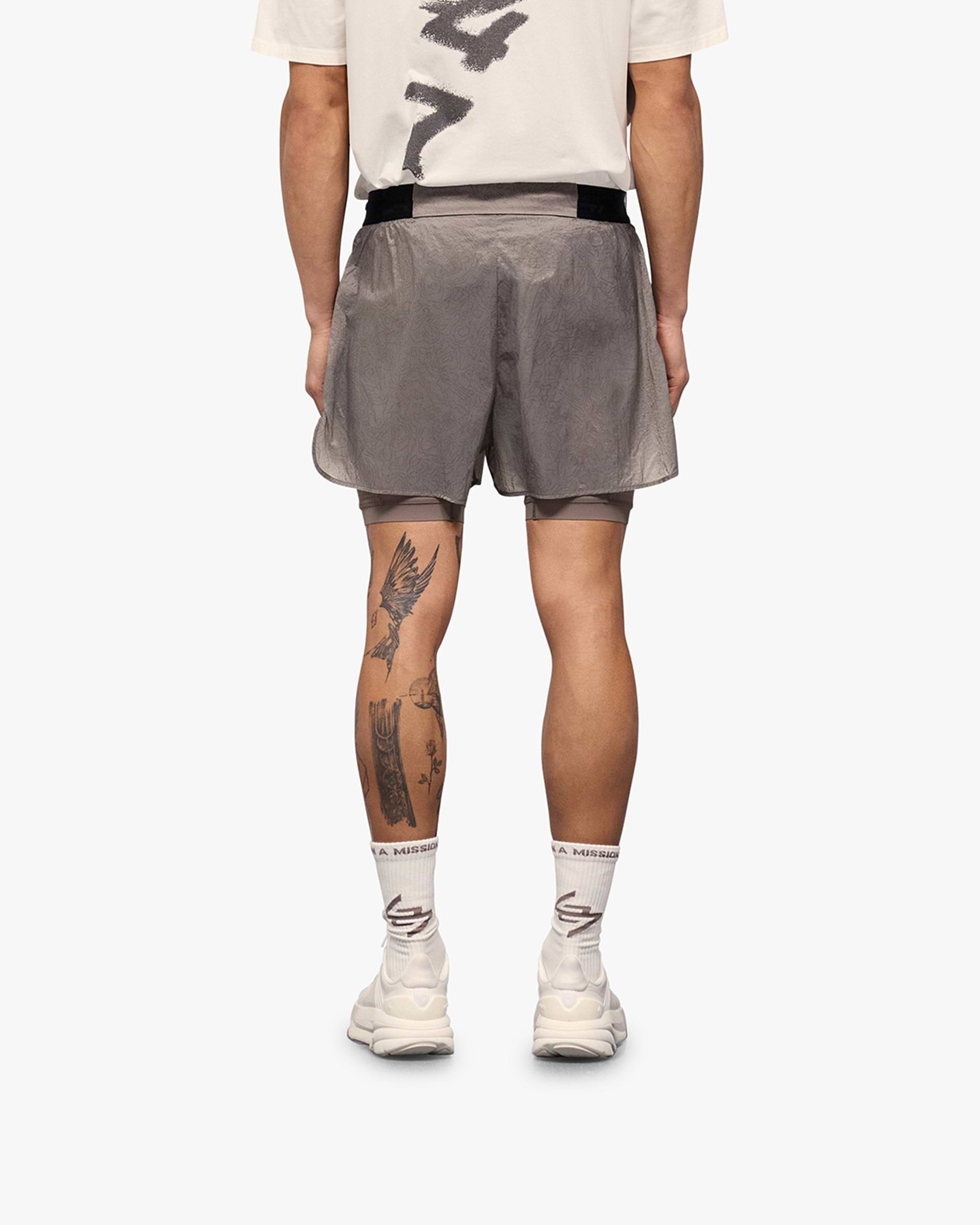 Man wearing grey shorts with inner leggings on a plain white background | 247 Contour 2-In-1 Run Shorts in Pebble | Shorts with drawcord and zip pockets | 247 Shorts | Represent Clo