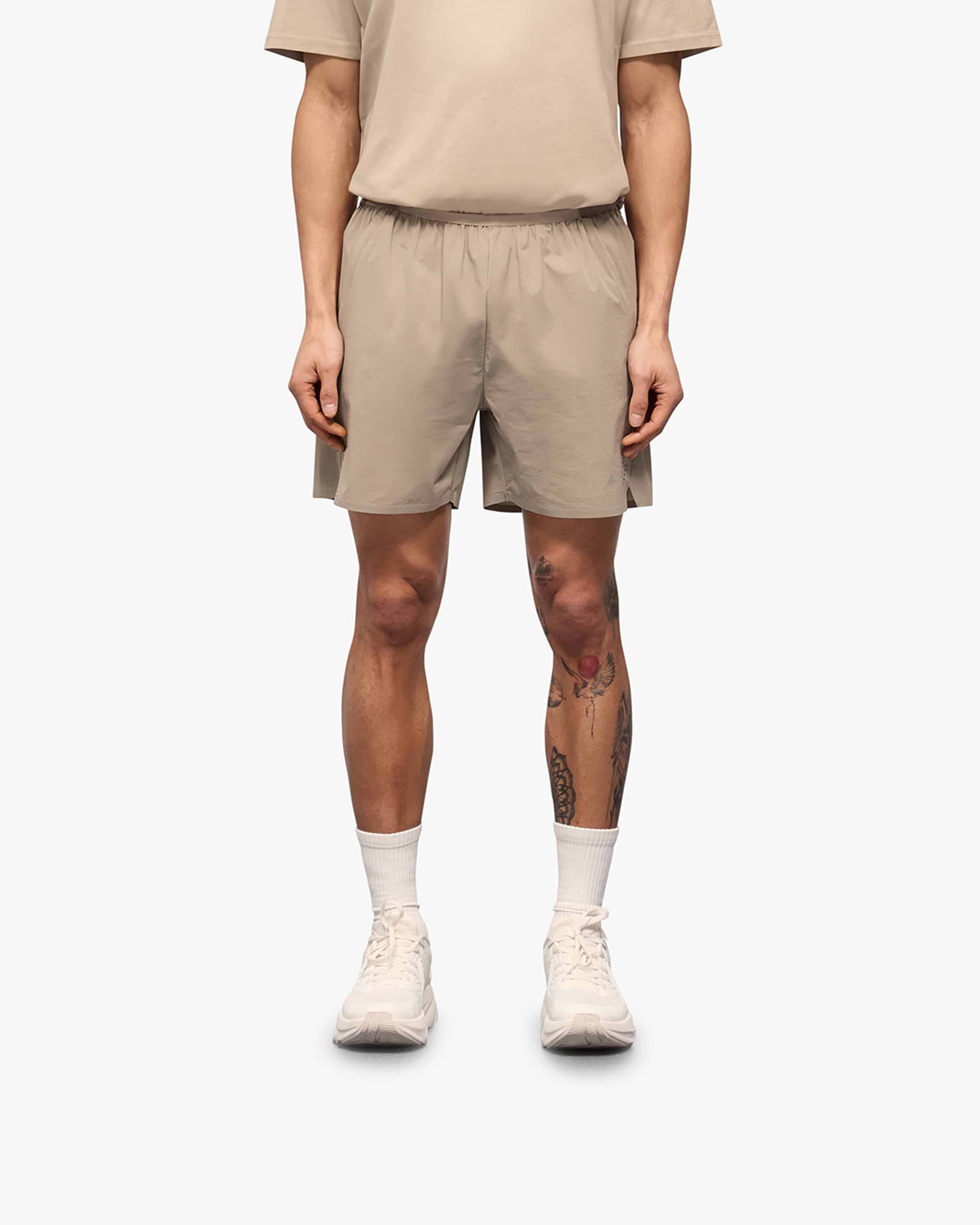 Man wearing grey shorts on a plain white background | 247 Training Shorts in Pebble | Nylon blend shorts with zip pockets and perforation detailing | 247 Shorts | Represent Clo