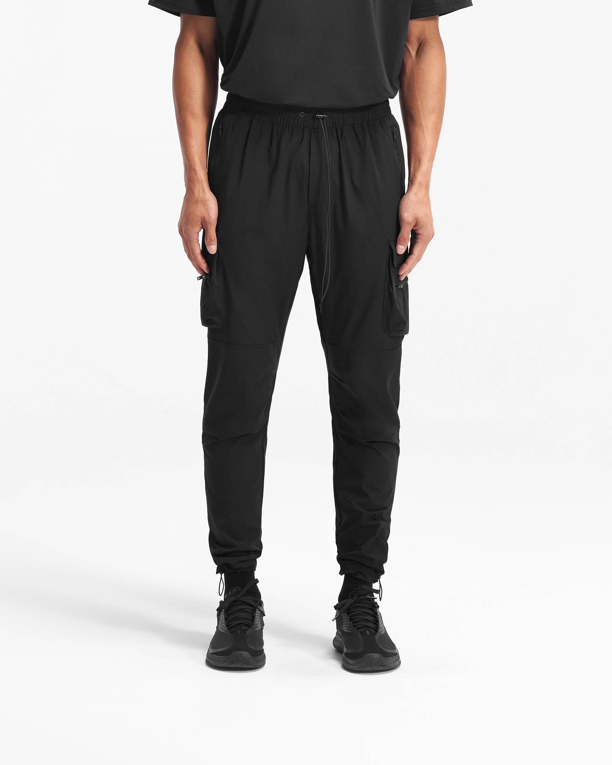 Man wearing black cargo pants on a plain white background | 247 Pant in Black | Technical 4-way stretch nylon cargo pants with zip side pockets | 247 Pants | Represent Clo