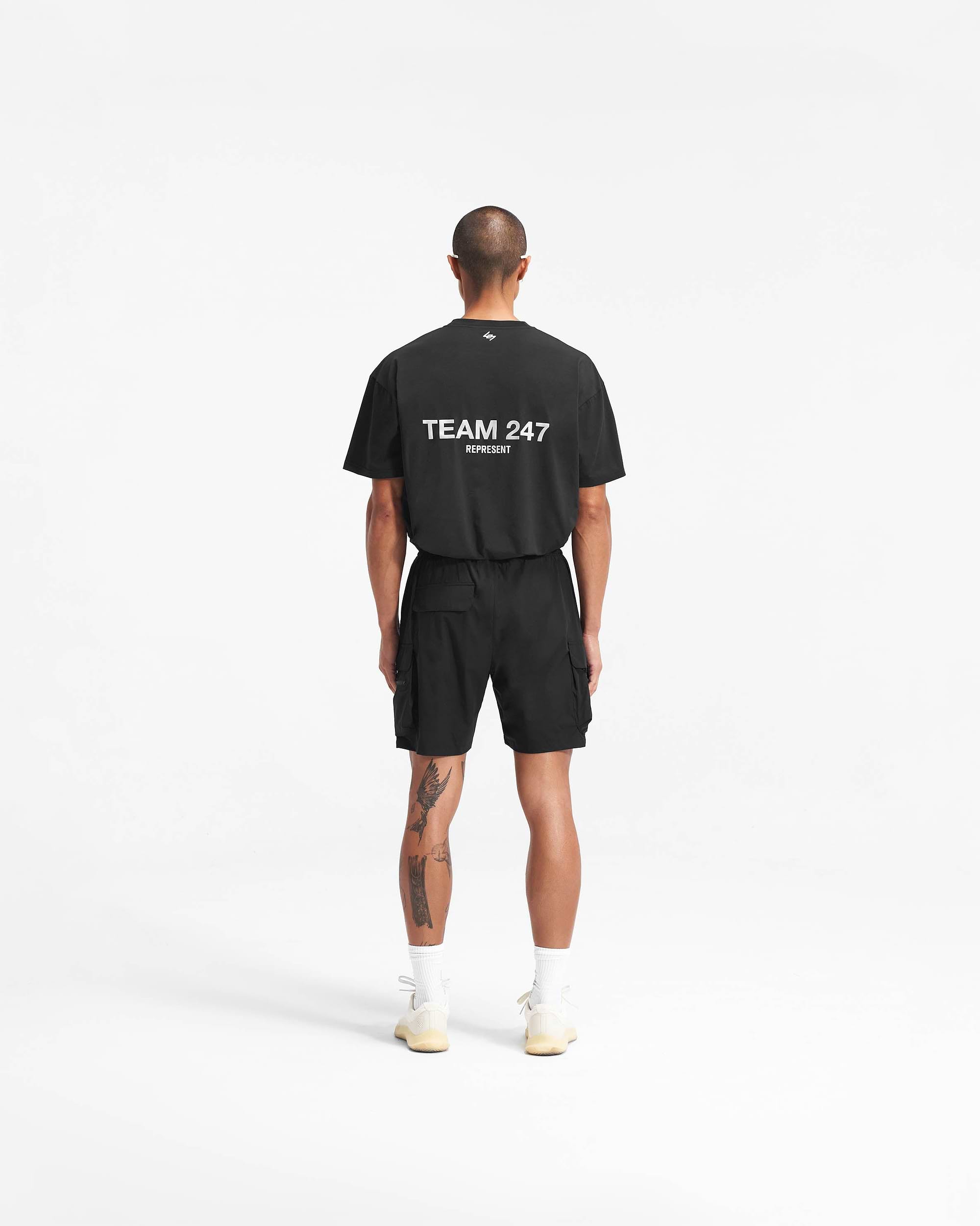 Man wearing black shorts on a plain white background | 247 Shorts in Black | Mens combat shorts with cargo leg pockets and zip side pockets | 247 Shorts | Represent Clo