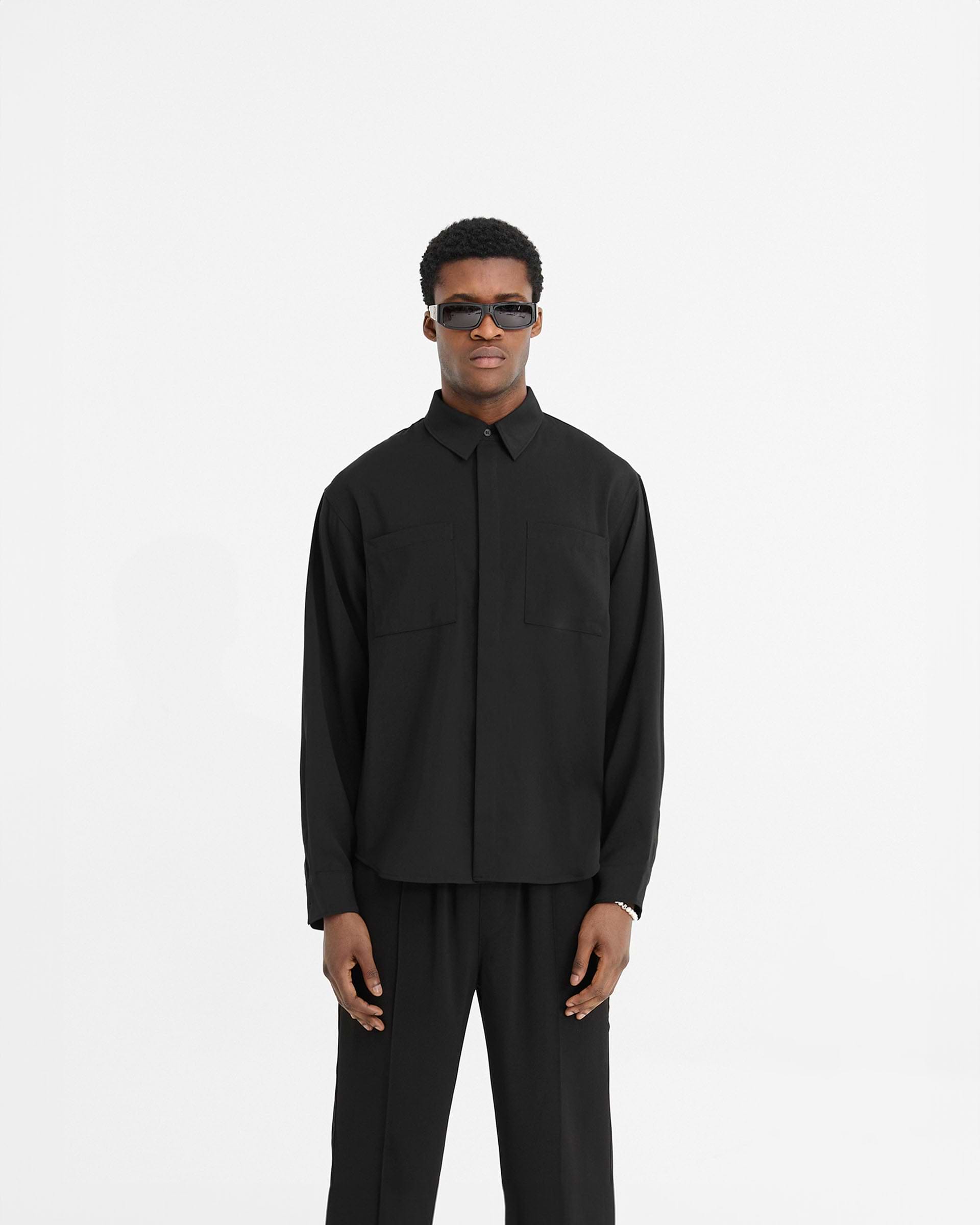 Man wearing a black shirt on a plain white background | Initial Shirt in Black | Slightly oversized black shirt with chest pockets and concealed placket | Initial Shirts | Represent Clo