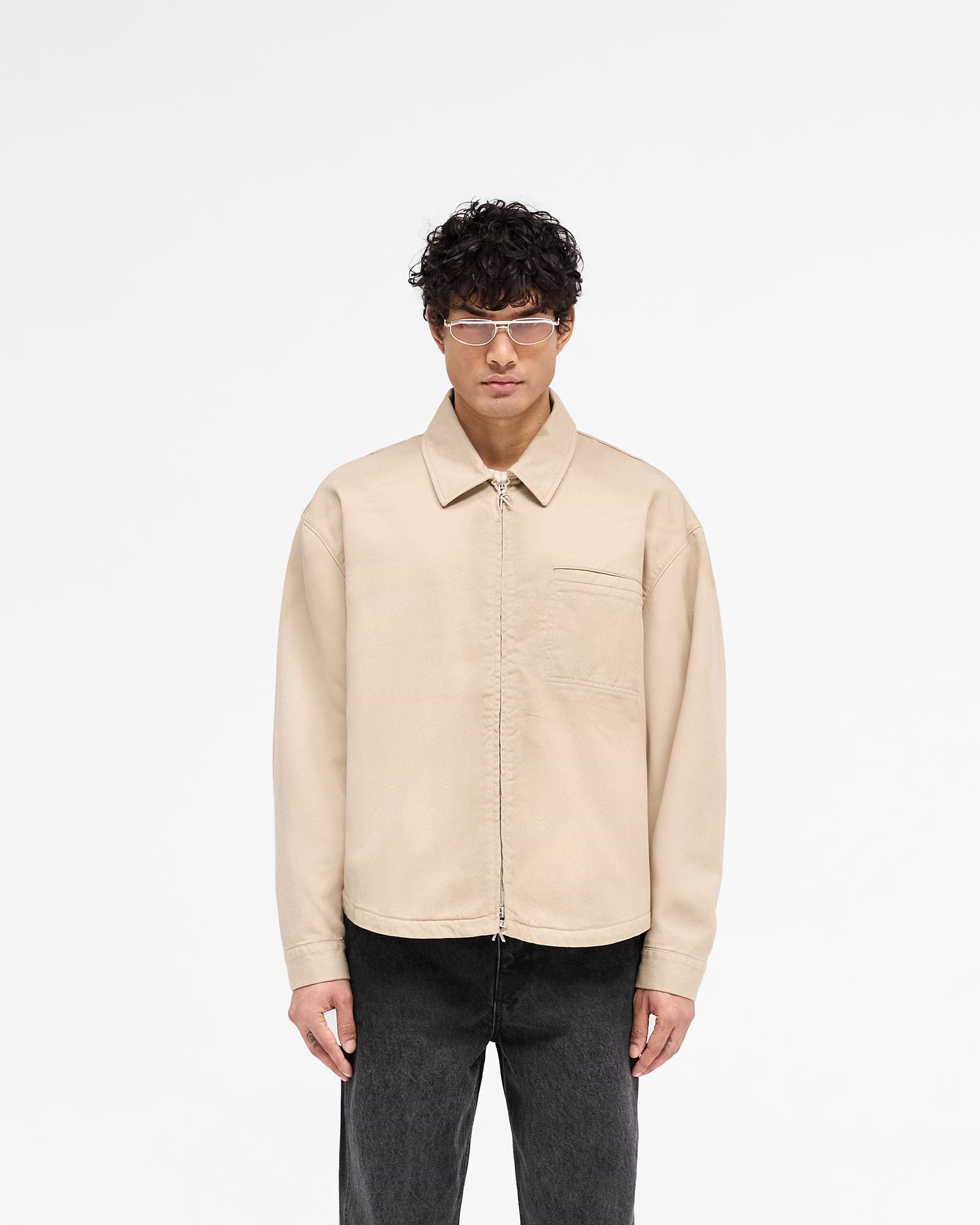 Man wearing a beige zip-through cotton shirt on a plain white background | Cotton Zip Through Shirt in Beige | Structured fit cotton twill shirt with double Represent zips and chest pocket | SS25 Shirts | Represent Clo