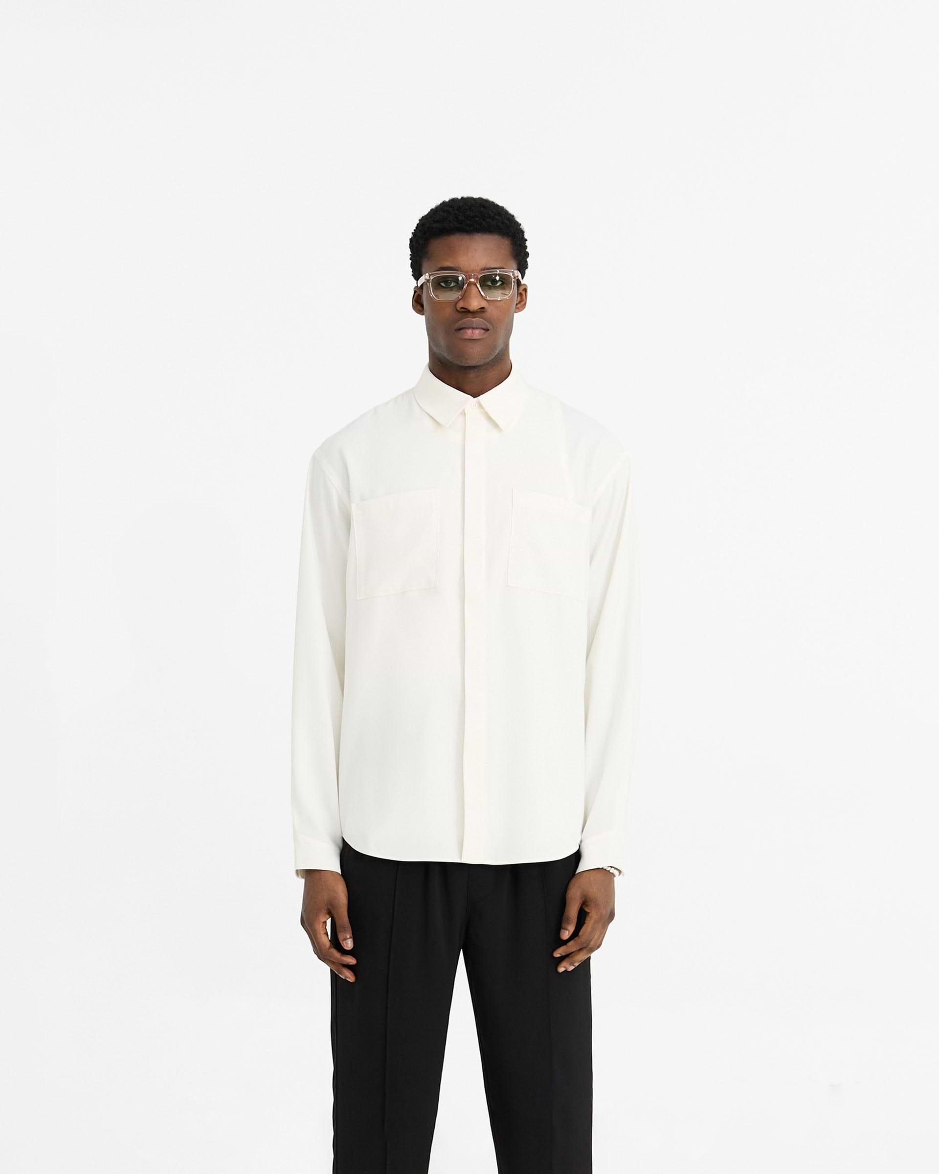 Man wearing a white shirt on a plain white background | Initial Shirt in Flat White | Drapey fabric oversized shirt with chest pockets | Initial Shirts | Represent Clo