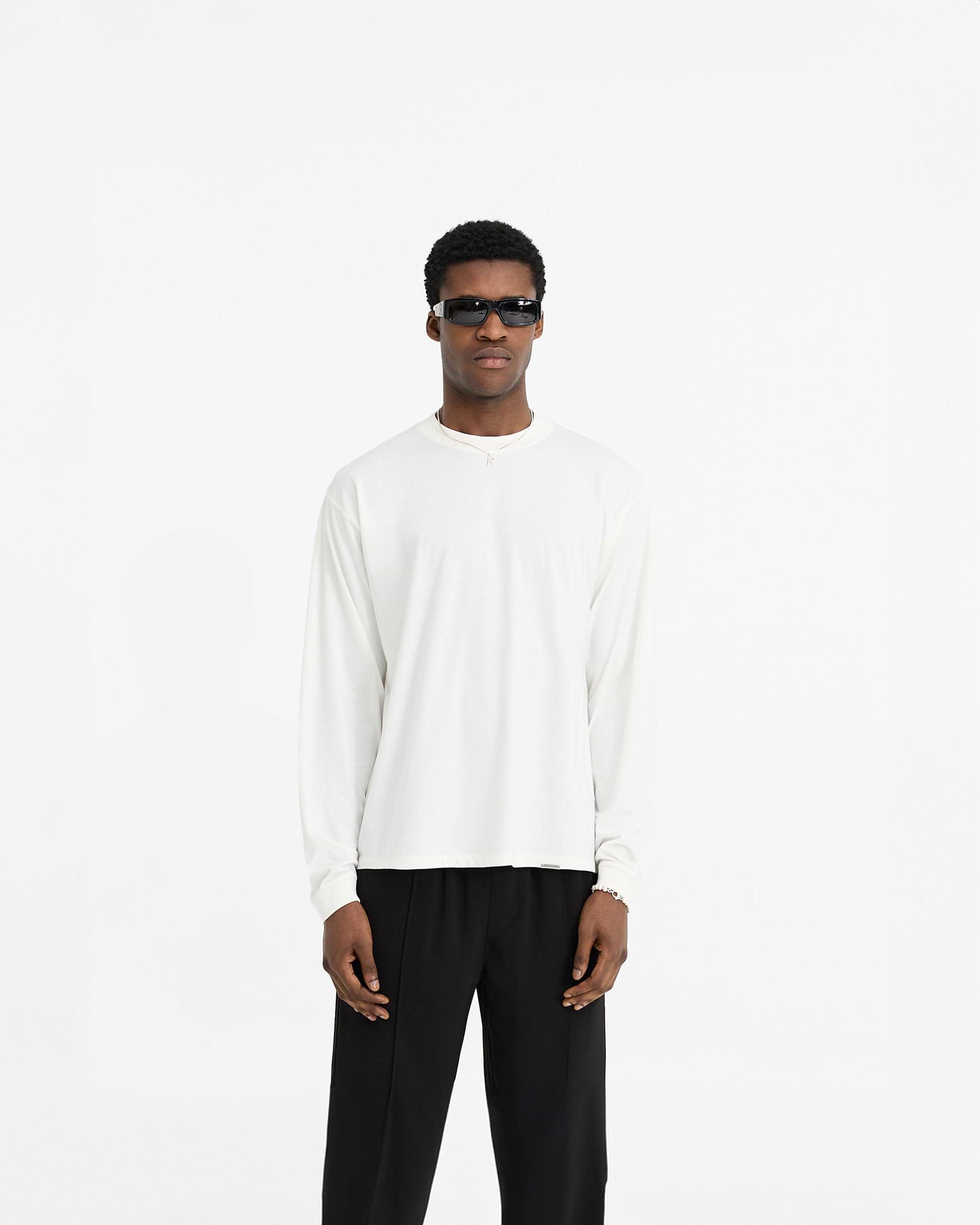 Man wearing a white long sleeve t-shirt on a plain white background | Initial Long Sleeve T-Shirt in Flat White | Jersey cotton long sleeve t-shirt with embroidered back neck | Initial T-Shirts | Represent Clo