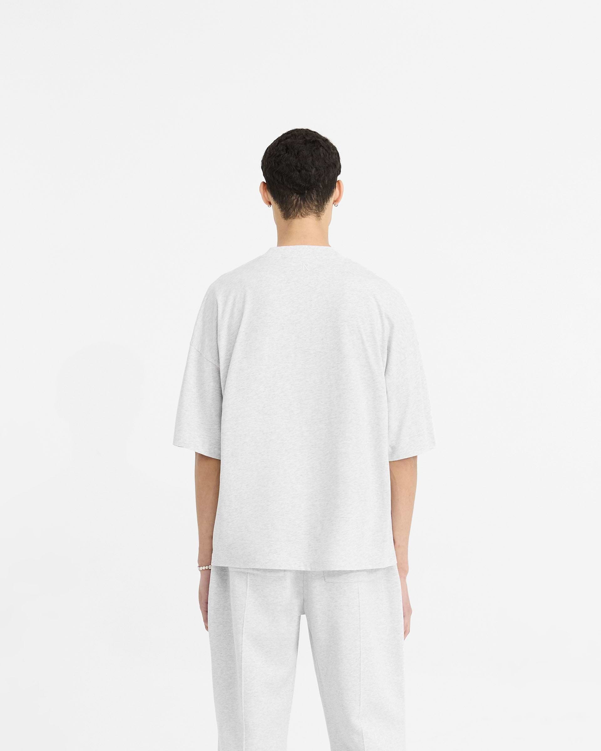 Man wearing a grey boxy t-shirt on a plain white background | Initial Boxy T-Shirt in Ice Grey Marl | Oversized cropped t-shirt with ribbed collar | Initial T-Shirts | Represent Clo