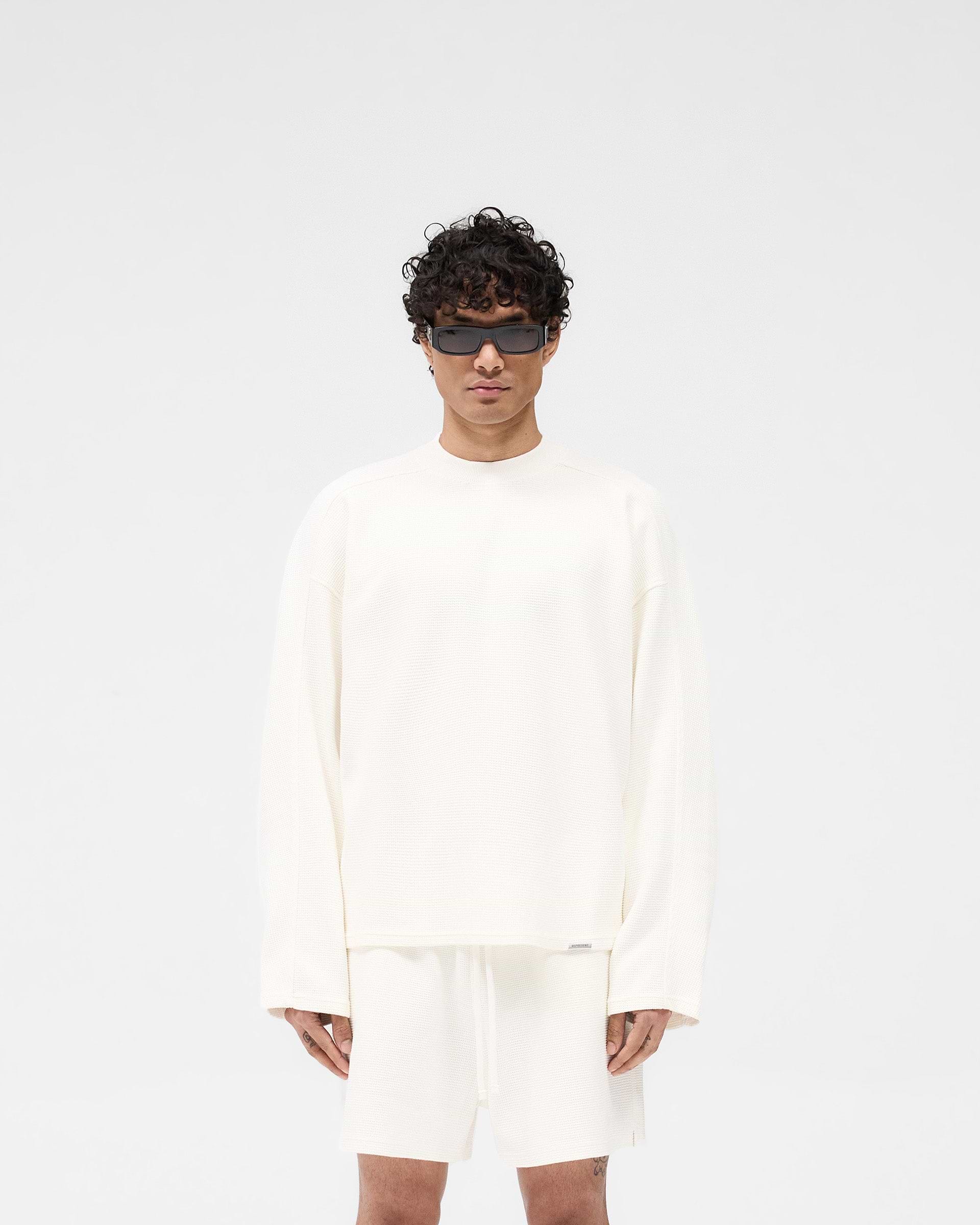 Man wearing a white long sleeve t-shirt on a plain white background | Waffle Long Sleeve T-Shirt in Flat White | Boxy fit waffle fabric t-shirt | SS25 T-Shirts | Represent Clo