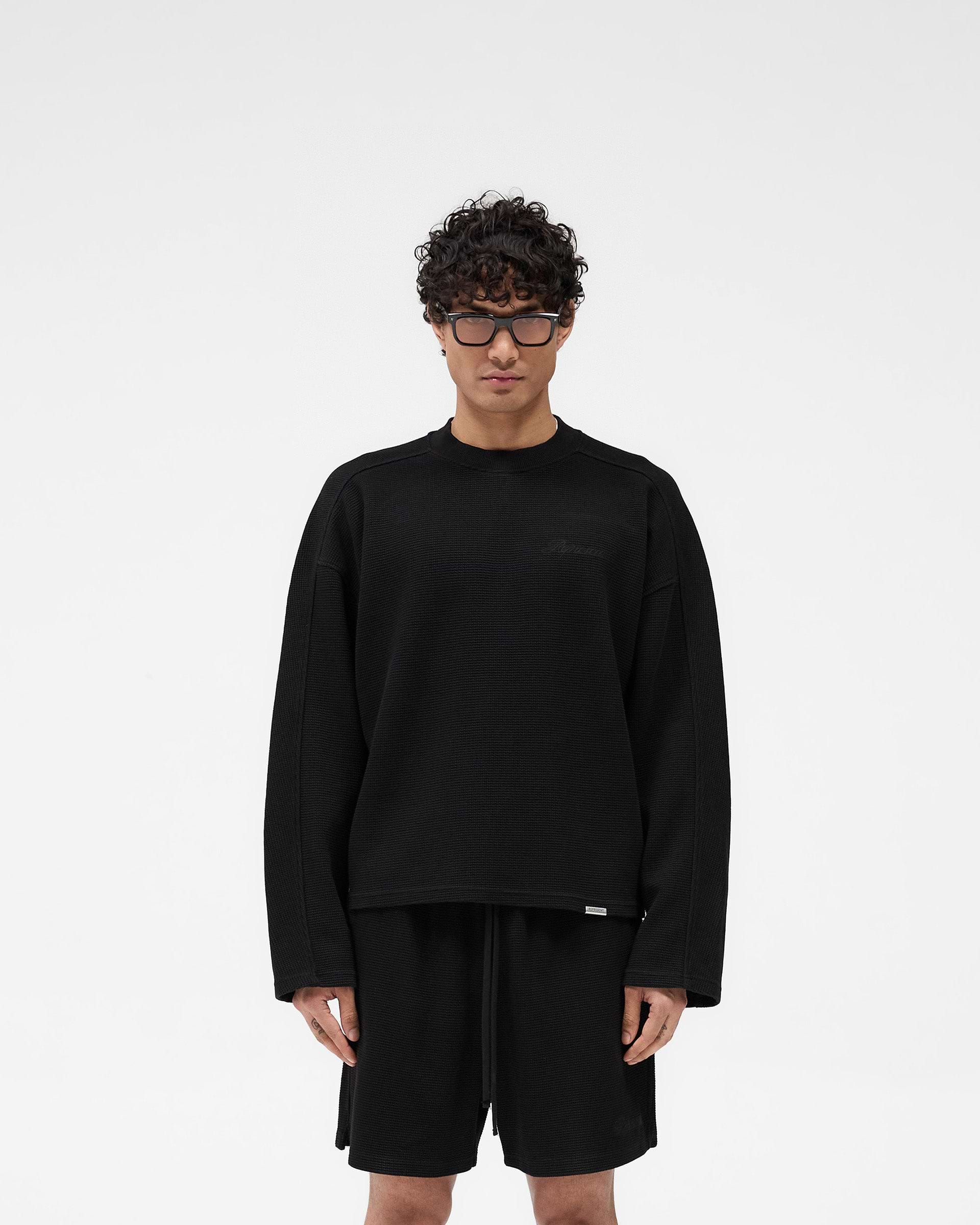 Man wearing a black long sleeve t-shirt on a plain white background | Waffle Long Sleeve T-Shirt in Black | Textured waffle fabric long sleeve T-shirt with boxy fit | SS25 T-Shirts | Represent Clo