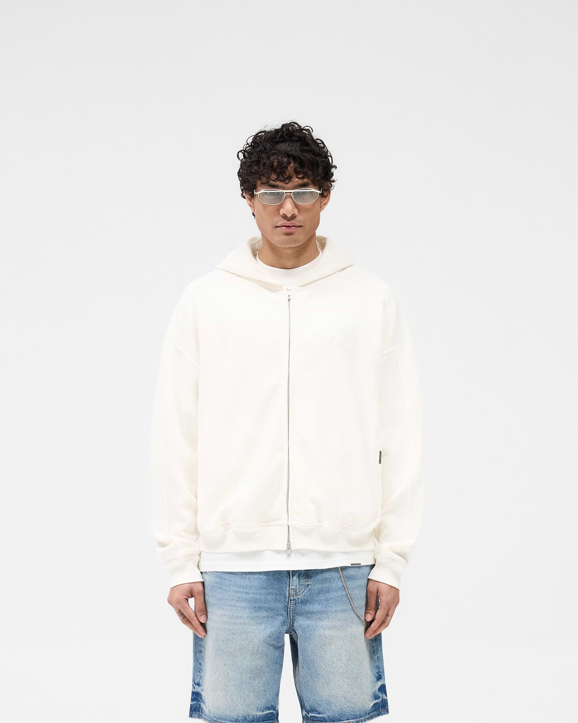 Man wearing an oversized white hoodie on a plain white background | Waffle Zip Through Hoodie in Flat White | Boxy fit hoodie with branded zipper and logo | SS25 Hoodies | Represent Clo