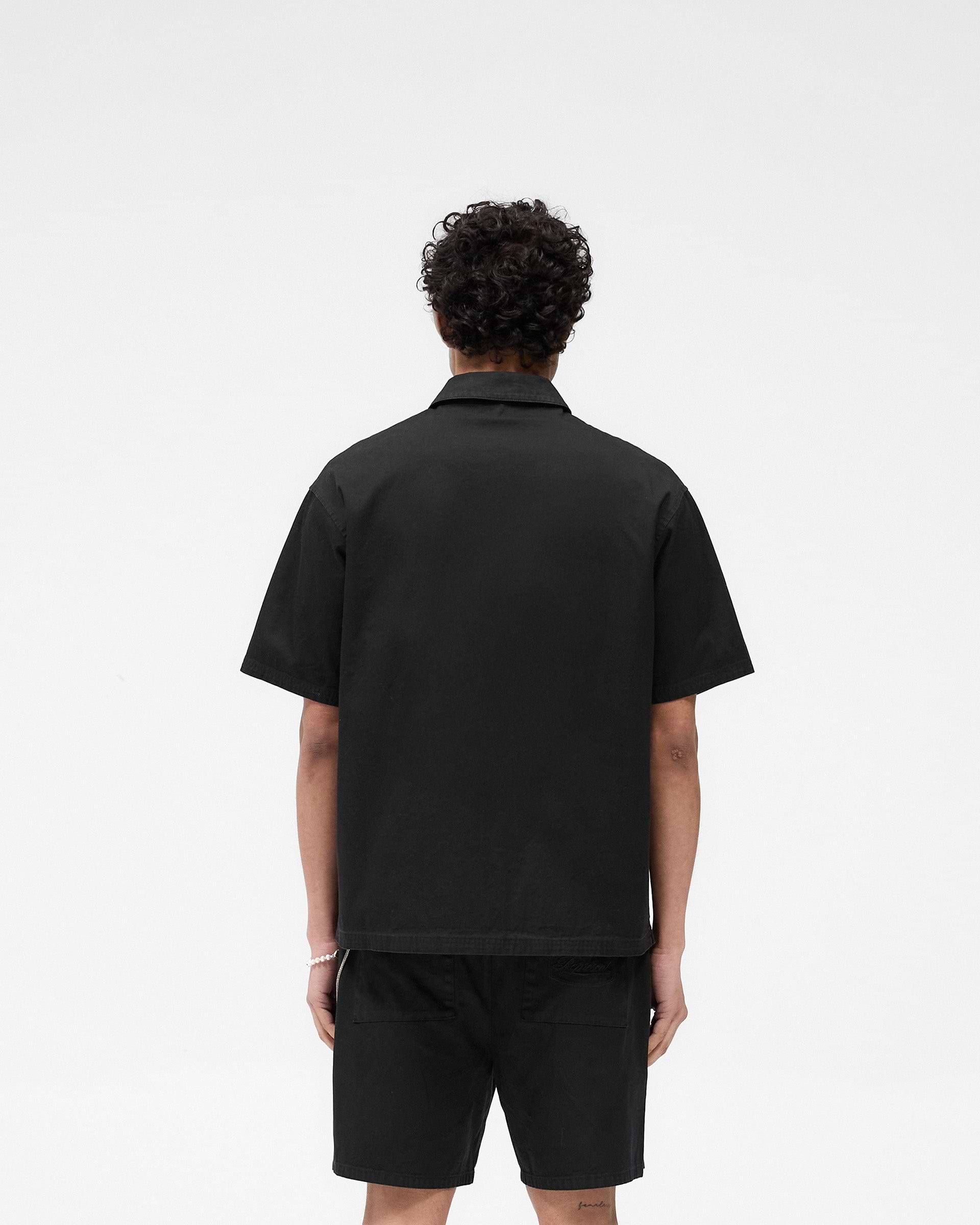 Man wearing a black cotton overshirt on a plain white background | Short Sleeve Cotton Overshirt in Washed Black | Overshirt with dual chest pockets | SS25 Shirts | Represent Clo