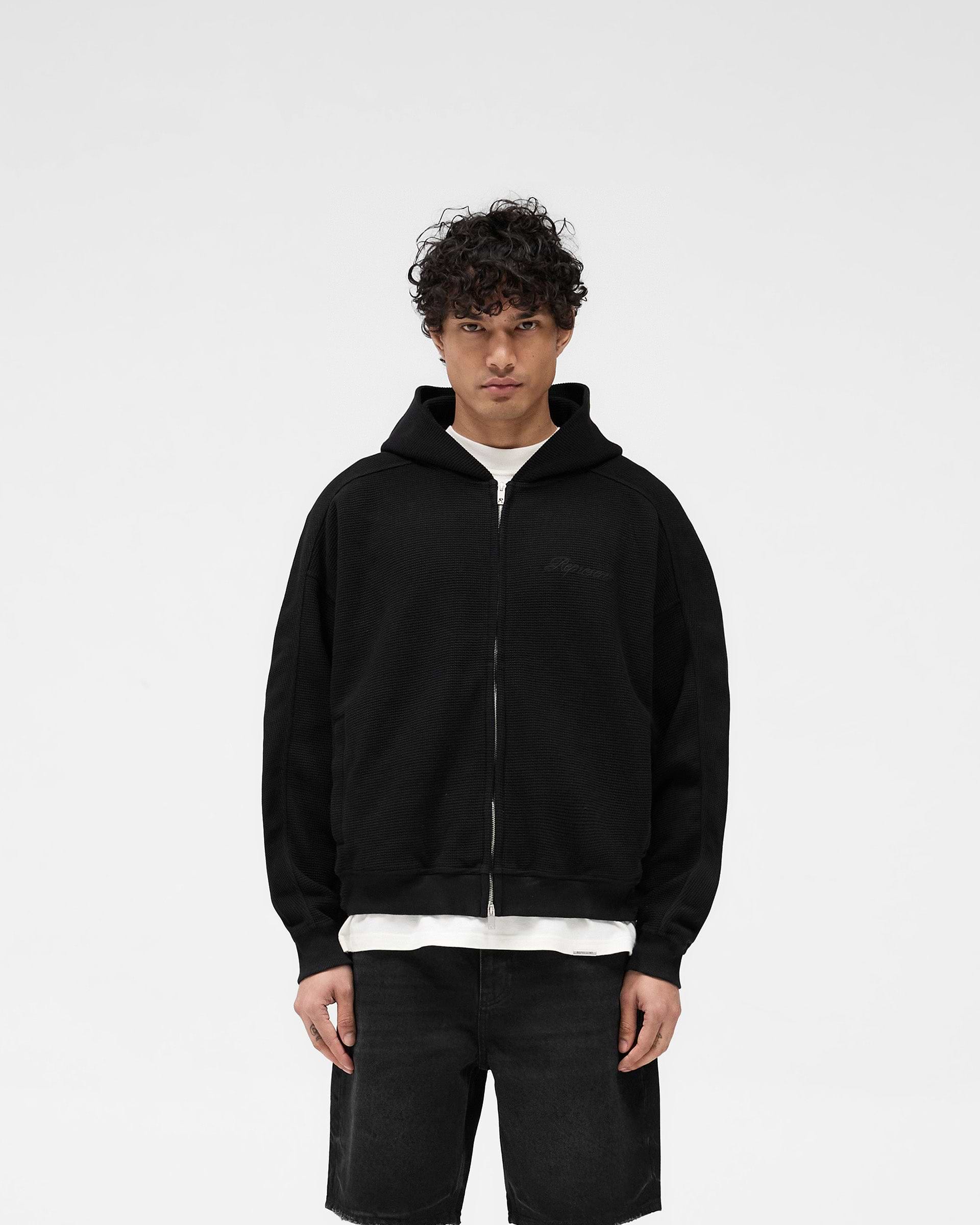 Man wearing a black oversized hoodie on a plain white background | Waffle Zip Through Hoodie in Jet Black | Boxy fit hoodie with chest embroidered logo and branded zipper | SS25 Hoodies | Represent Clo