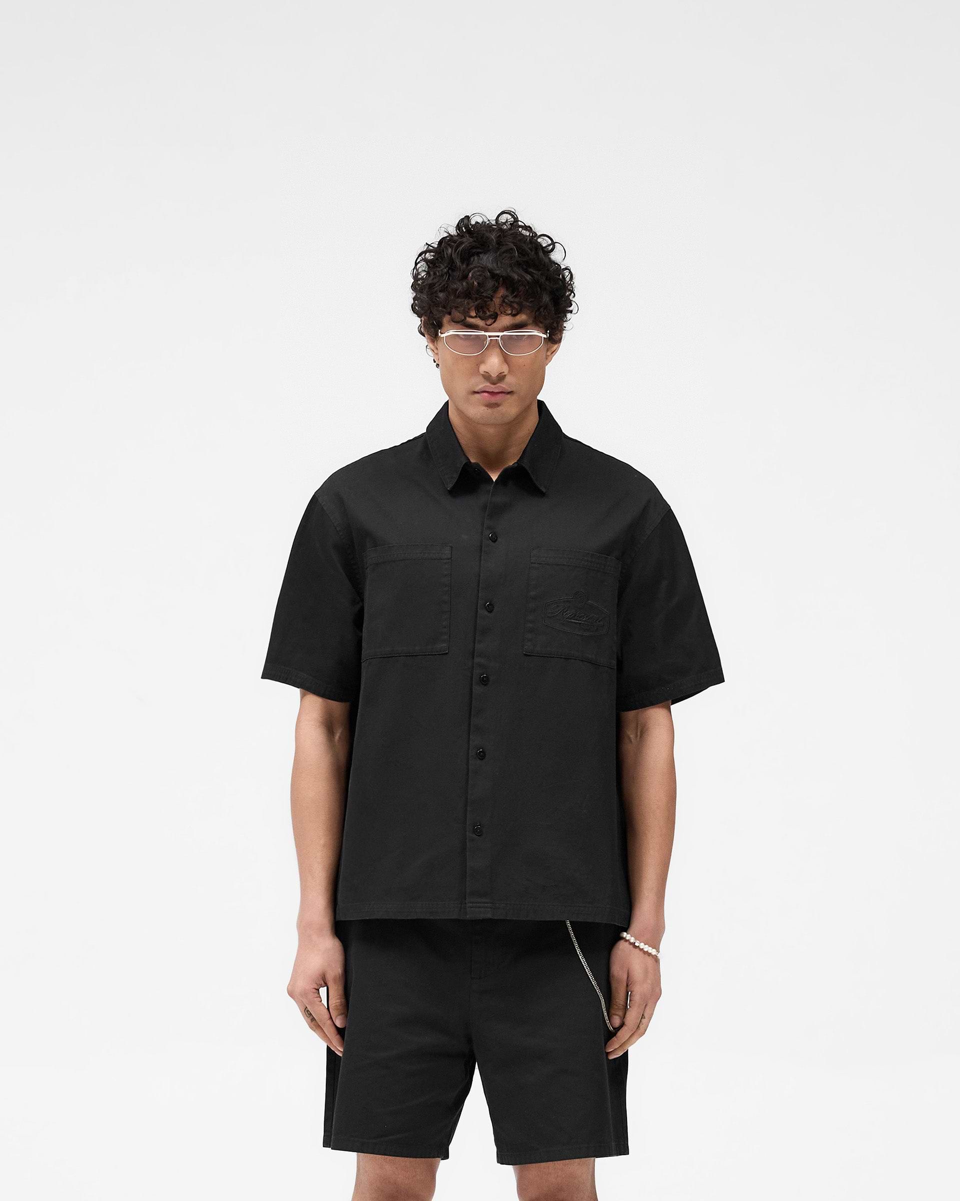 Man wearing a short-sleeve black overshirt on a plain white background | Short Sleeve Cotton Overshirt in Washed Black | Boxy fit with dual chest pockets | SS25 Shirts | Represent Clo