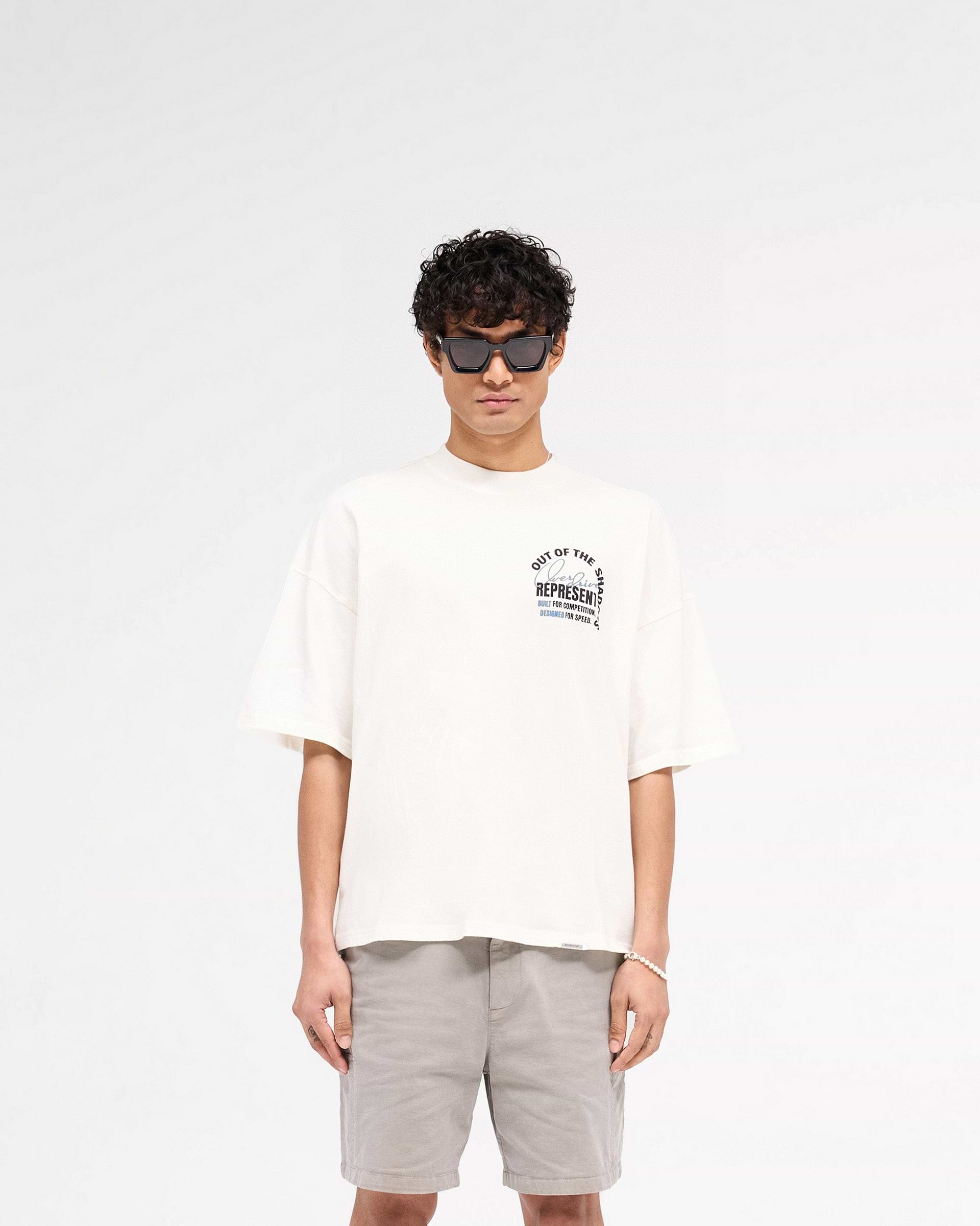 Man wearing a flat white t-shirt on a plain white background | Out Of The Shadows T-Shirt in Flat White | Boxy fit t-shirt with high build print | SS25 T-Shirts | Represent Clo