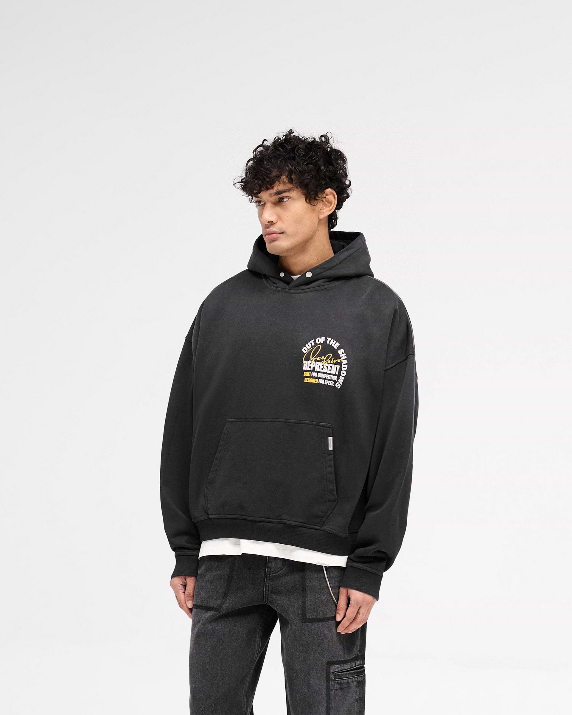 Man wearing a black hoodie on a plain white background | Out Of The Shadows Hoodie in Stained Black | Oversized boxy fit hoodie with Cobrax popper and metal logo | SS25 Hoodies | Represent Clo