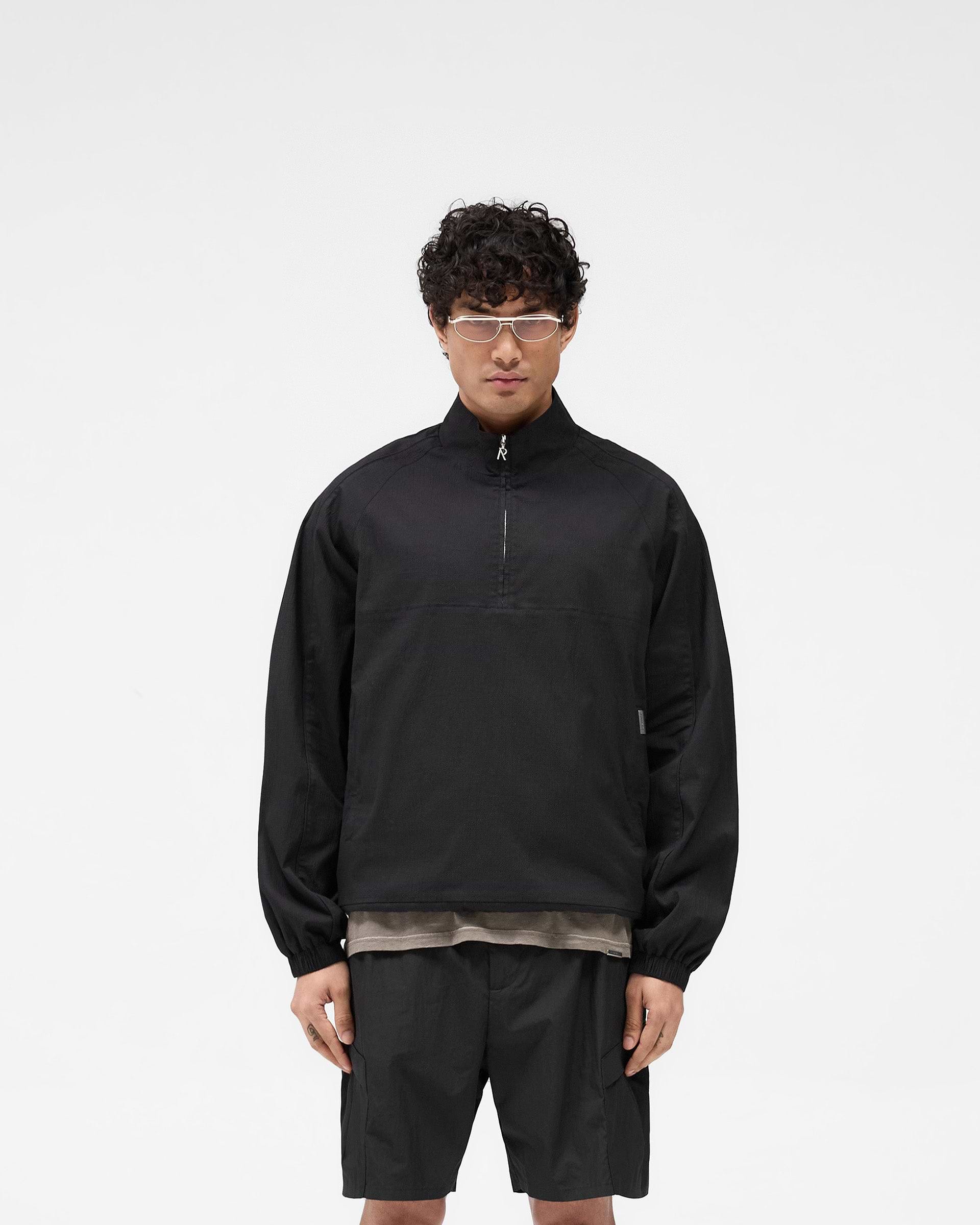 Man wearing a black quarter zip jacket on a plain white background | Quarter Zip Jacket in Black | Lightweight oversized outerwear with elasticated cuffs | SS25 Outerwear | Represent Clo