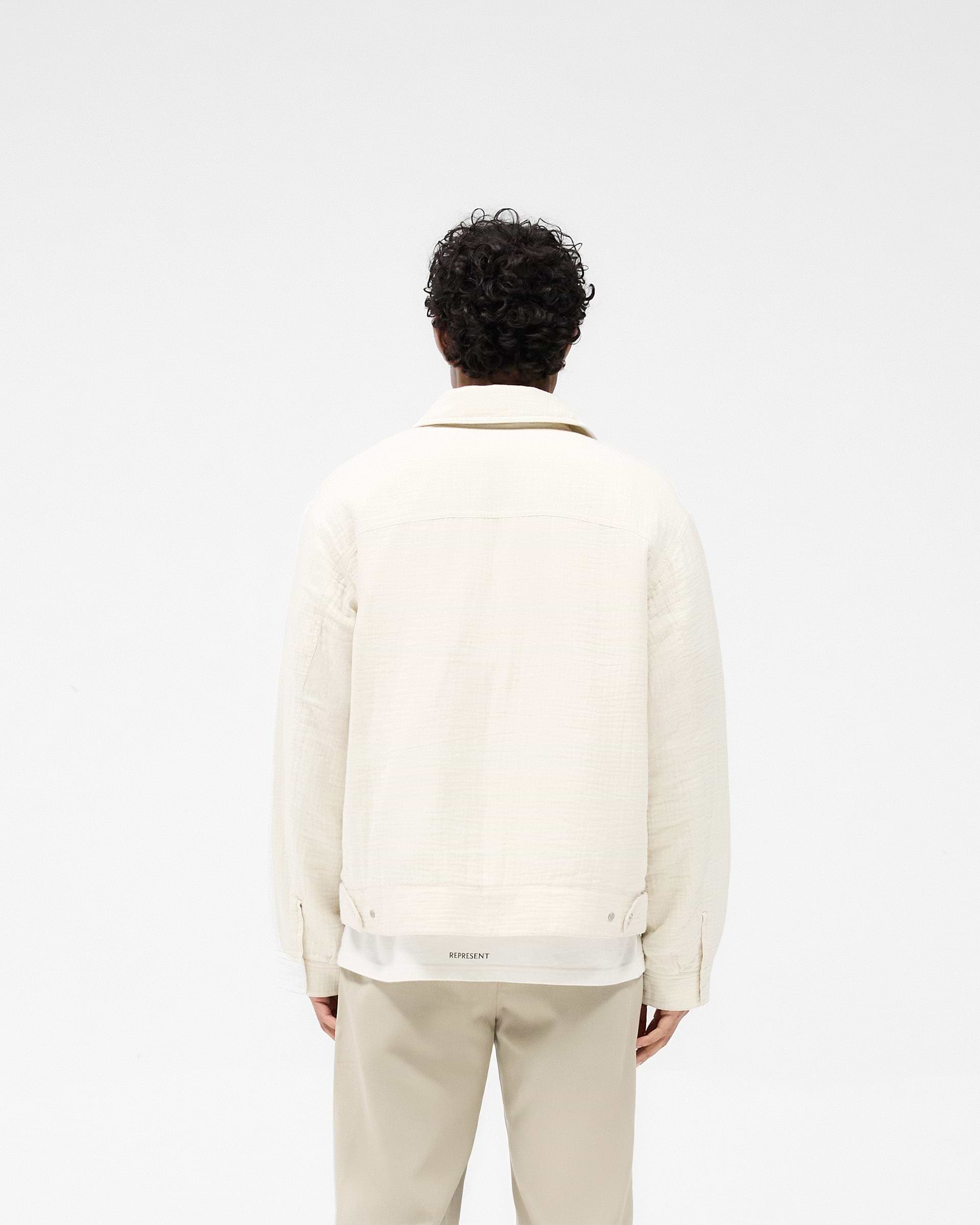 Man wearing an ecru trucker jacket on a plain white background | Crinkle Trucker Jacket in Ecru | Oversized cotton trucker jacket with charm zip | SS25 Outerwear | Represent Clo
