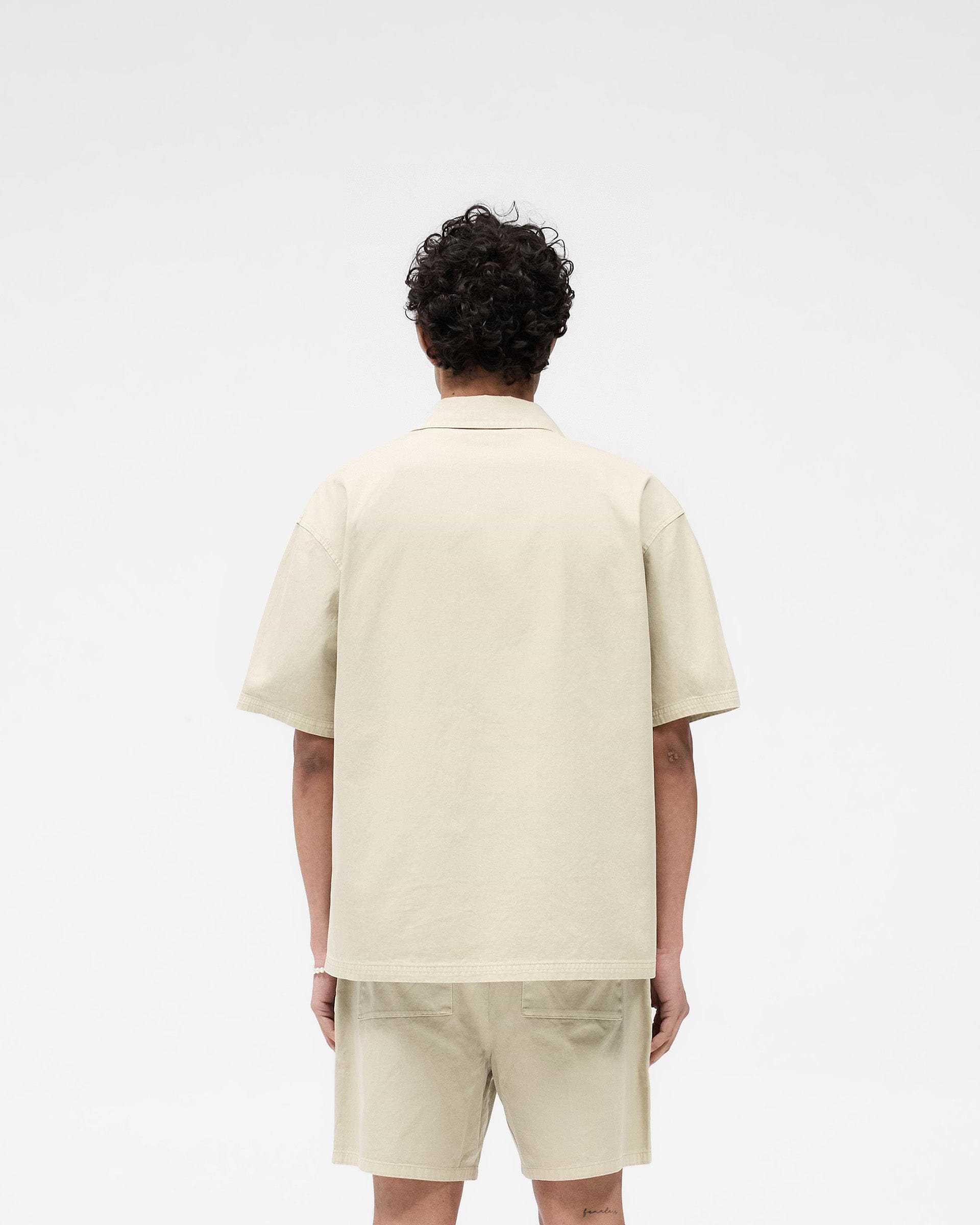 Man wearing a beige short sleeve overshirt on a plain white background | Short Sleeve Cotton Overshirt in Beige | Heavyweight twill with button-front and crest embroidery | SS25 Shirts | Represent Clo