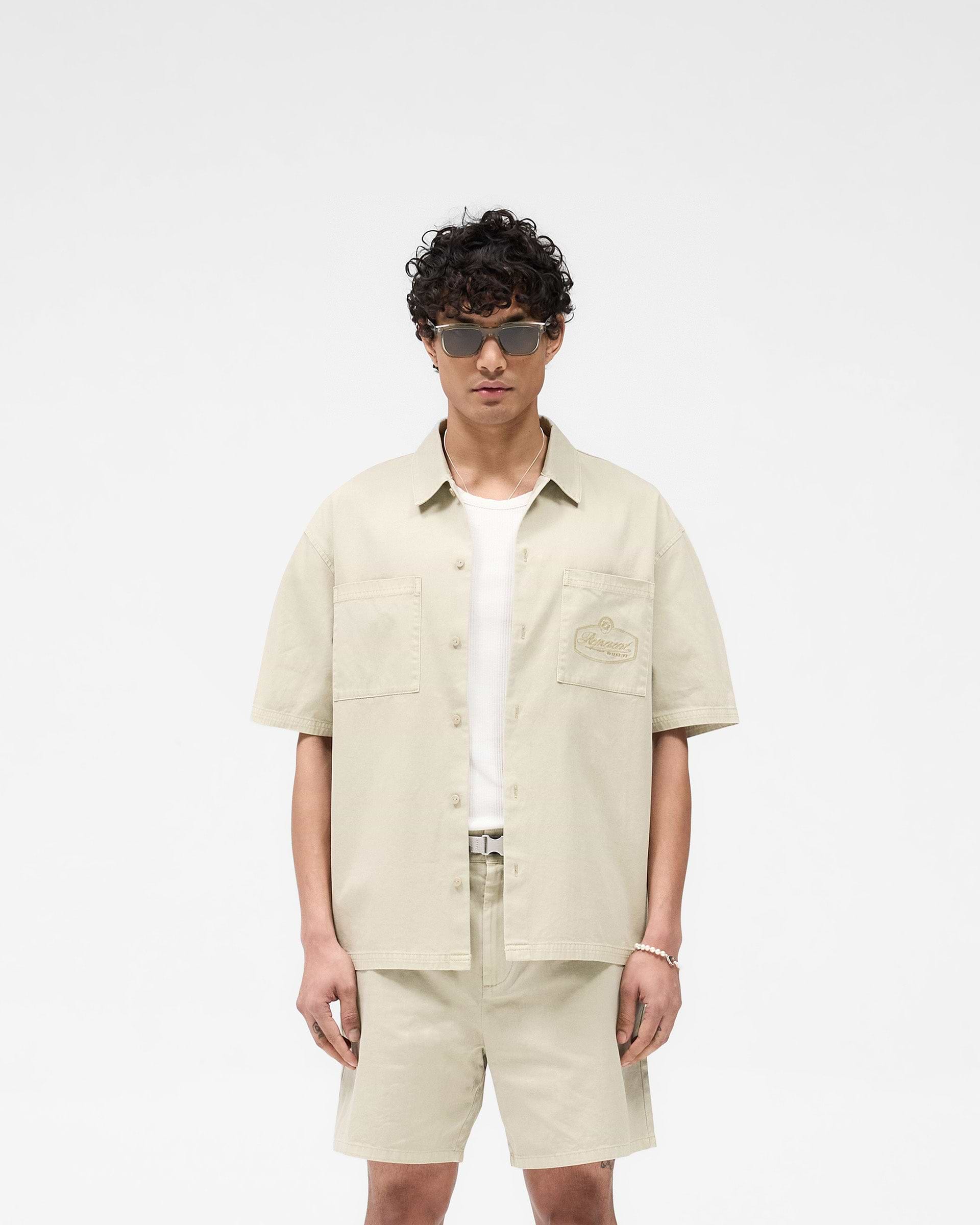 Man wearing a beige short sleeve overshirt on a plain white background | Short Sleeve Cotton Overshirt in Beige | Rigid twill with dual chest pockets | SS25 Shirts | Represent Clo