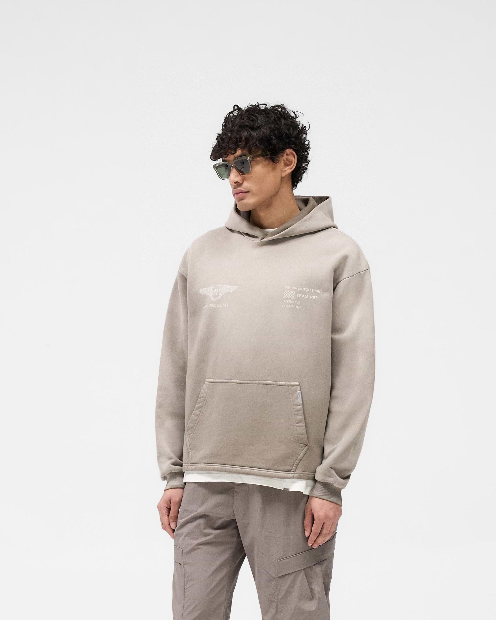 Man wearing an oversized dark taupe hoodie on a plain white background | Team Rep Hoodie in Dark Taupe | Oversized hoodie with vintage graphic | SS25 Hoodies | Represent Clo