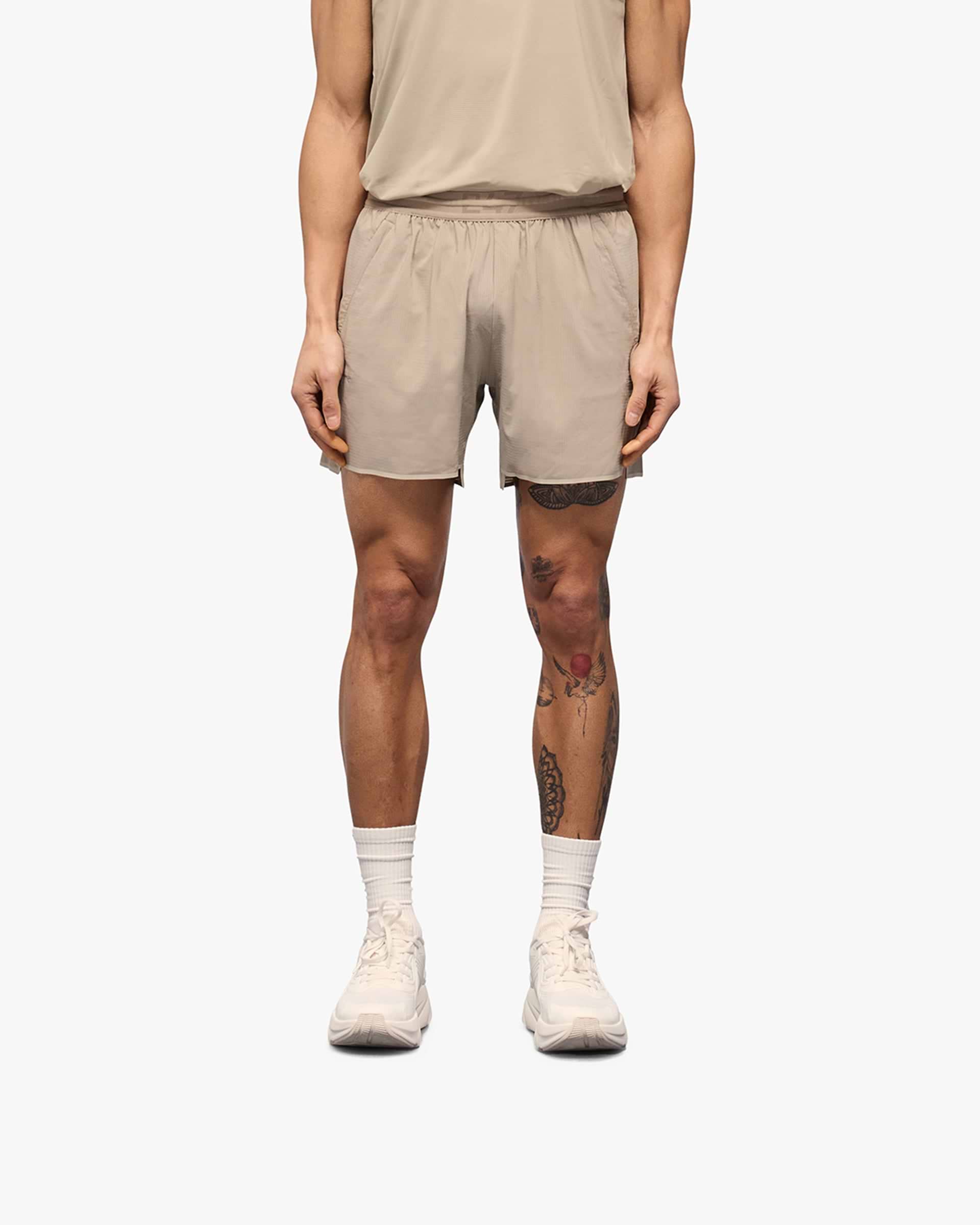 Man wearing grey shorts on a plain white background | Team 247 Aero Shorts in Pebble | Lightweight running shorts with branded waistband and zip pockets | 247 Shorts | Represent Clo