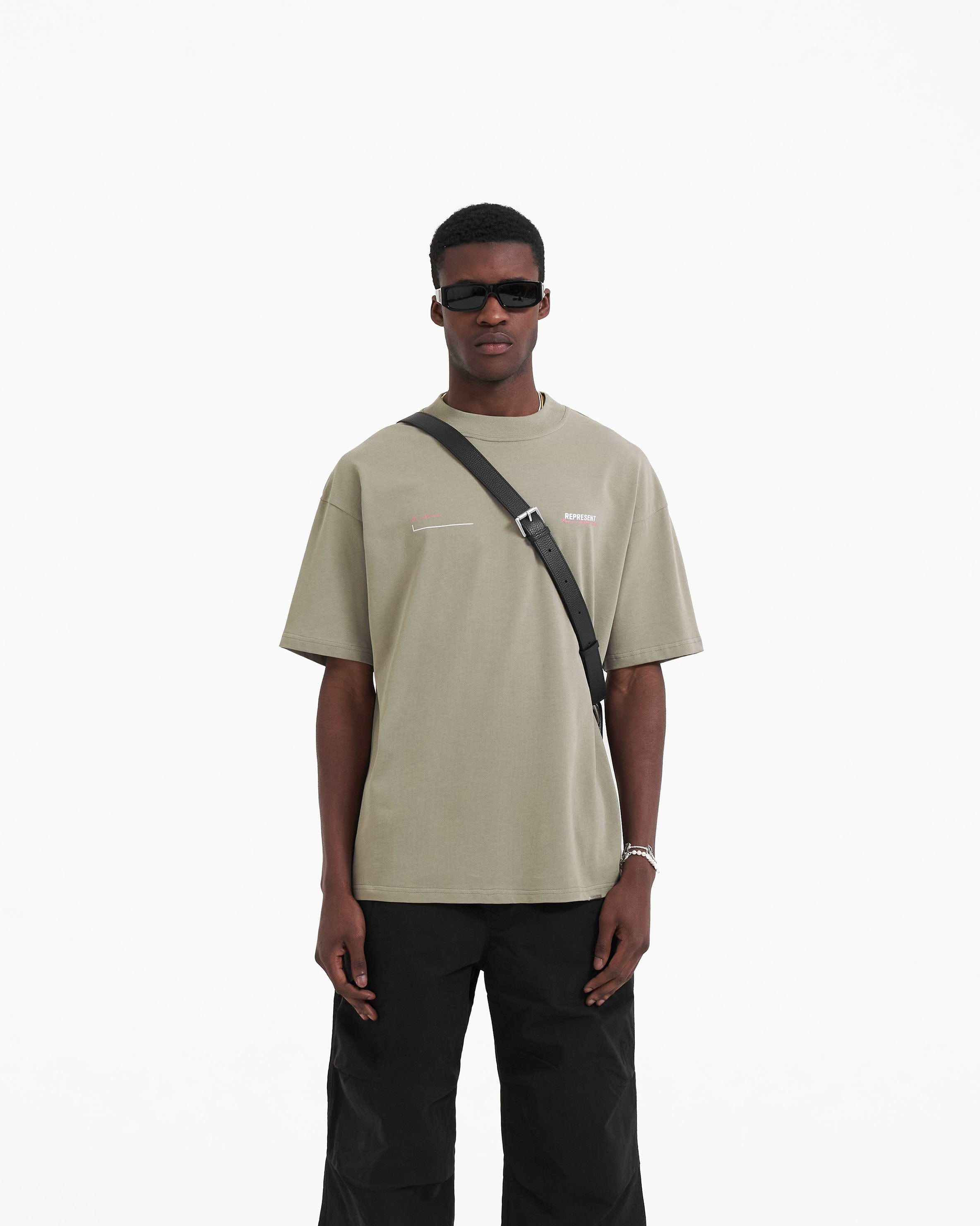 Man wearing a khaki t-shirt on a plain white background | Patron Of The Club T-Shirt in Khaki Pink | Oversized fit cotton t-shirt with screen print | Patrons T-Shirts | Represent Clo