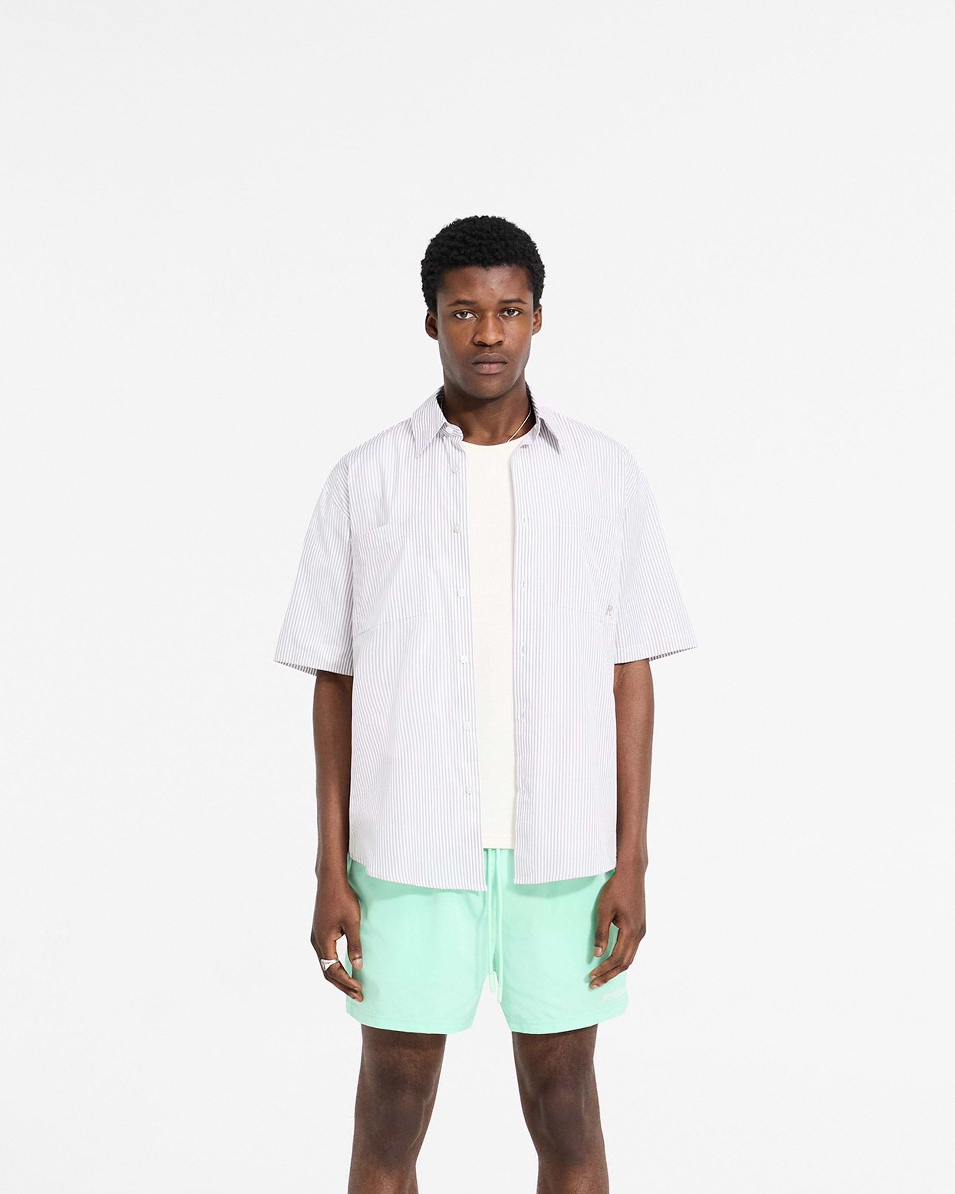 Man wearing a grey pinstripe shirt on a plain white background | Short Sleeve Pinstripe Shirt in Grey | Slightly oversized shirt with curved hem and chest pockets | SC24 Shirts | Represent Clo