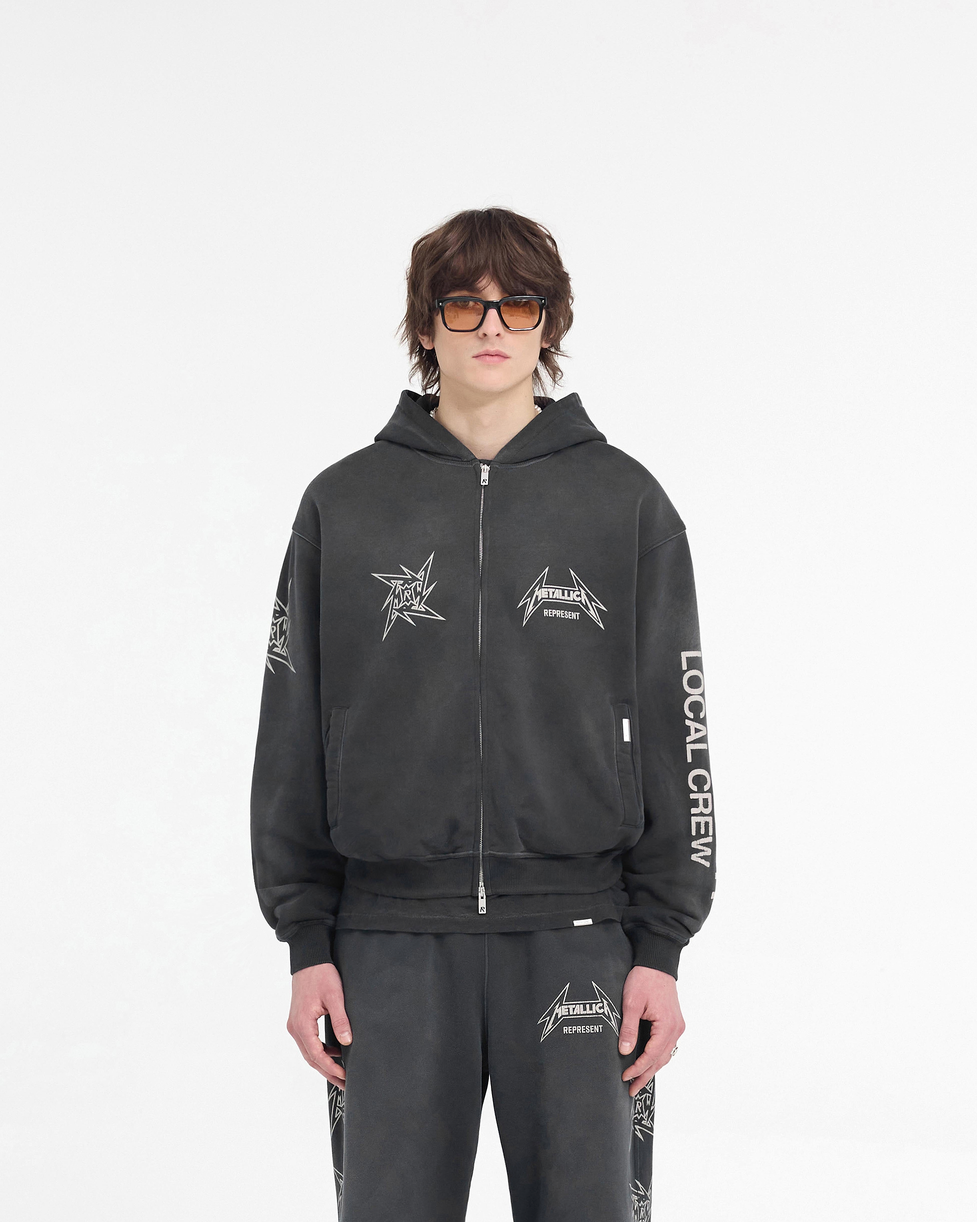 Man wearing a black zip hoodie on a plain white background | Represent X Metallica Local Crew Zip Hoodie in Stained Black | Slightly oversized hoodie with cracked graphics | SS24 Hoodies | Represent Clo