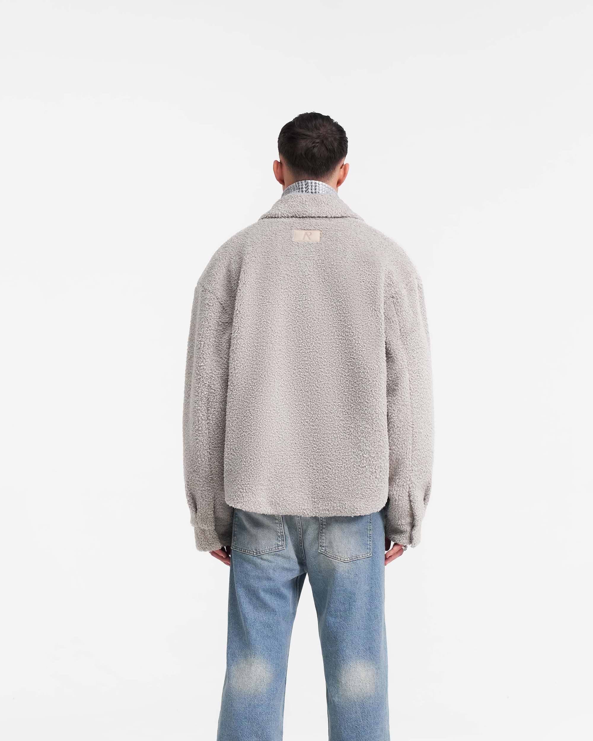 Man wearing a grey shearling shirt on a plain white background | Shearling Scoop Hem Shirt in Ice Grey | Shearling shirt with zip and popper closure | PRE SS24 Shirts | Represent Clo