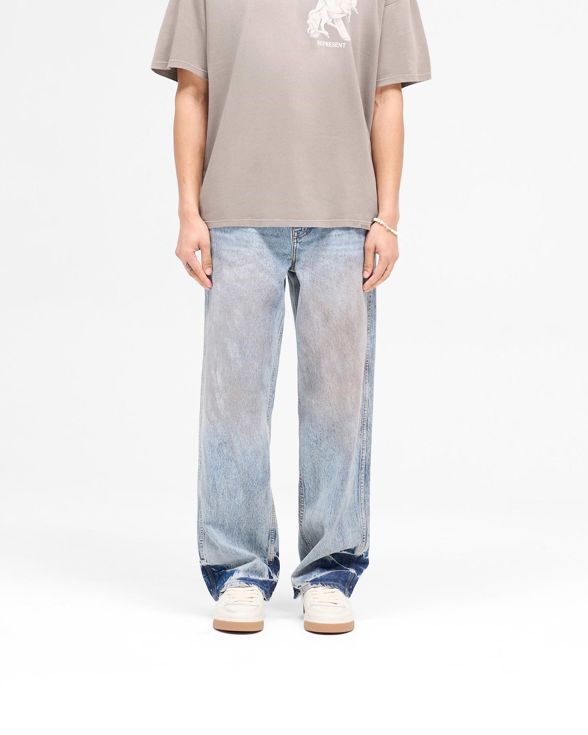 Man wearing mens blue denim jeans on a plain white background | R3 Baggy Denim in Mechanic Blue | Baggy fit jeans with patched dye and signature embroidery | SS25 Denim | Represent Clo