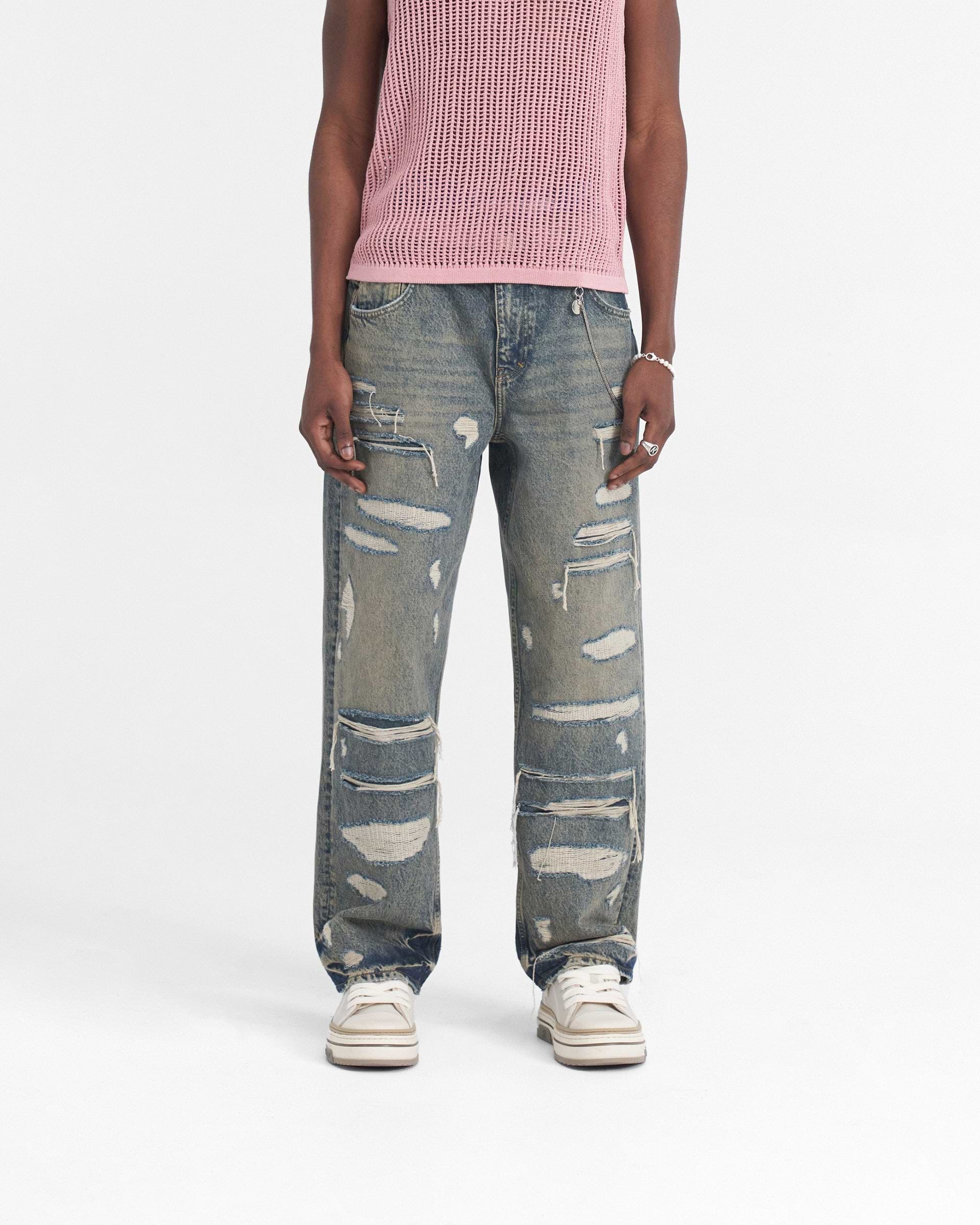 Man wearing blue cream baggy denim jeans with heavy distressed rips on a plain white background | R3D Double Destroyer Baggy Denim in Blue Cream | Relaxed fit denim with embroidered detail | SS24 Denim | Represent Clo