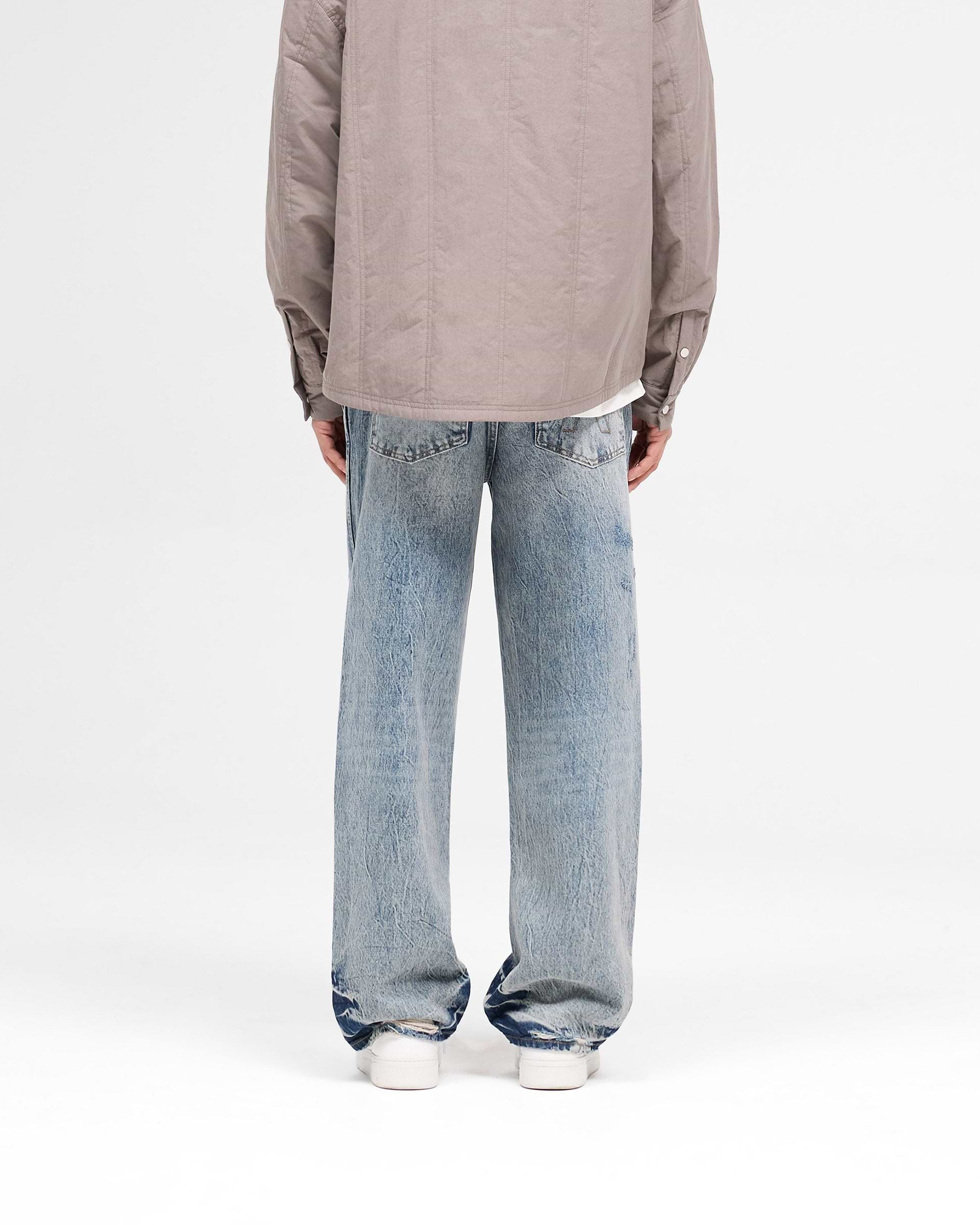Man wearing distressed baggy denim jeans in blue cream on a plain white background | R3 Distressed Baggy Denim in Blue Cream | Relaxed fit denim with rips and signature Initial embroidery | SS25 Denim | Represent Clo