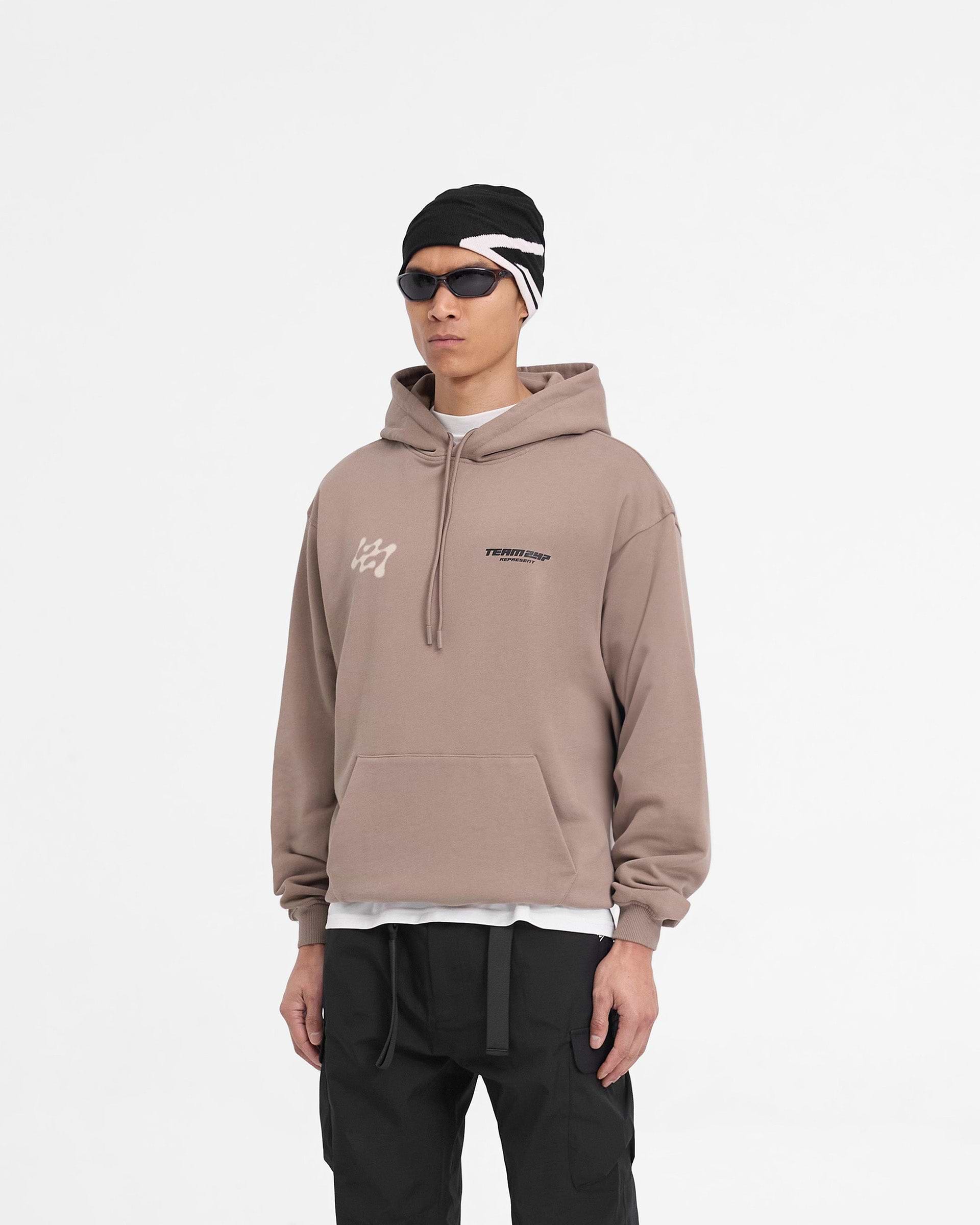 Man wearing an oversized brown hoodie on a plain white background | 247 Future Terrains Oversized Hoodie in Umber | Heavyweight hoodie with ribbed hem and cuffs | 247 Hoodies | Represent Clo