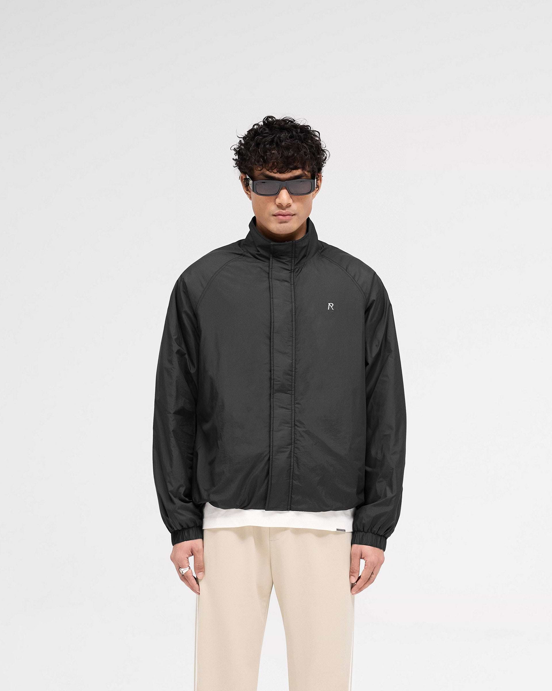 Man wearing a black jacket on a plain white background | Funnel Neck Jacket in Black | Lightweight nylon outer with funnel neck and raglan sleeves | SS25 Outerwear | Represent Clo