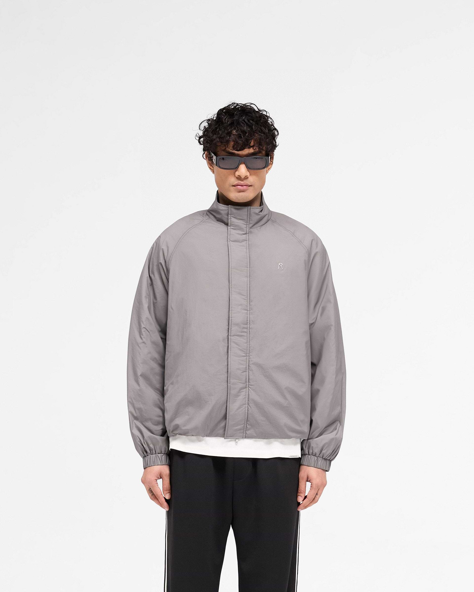 Man wearing a stone jacket on a plain white background | Funnel Neck Jacket in Stone | Lightweight jacket with funnel neck and elasticated cuffs | SS25 Outerwear | Represent Clo